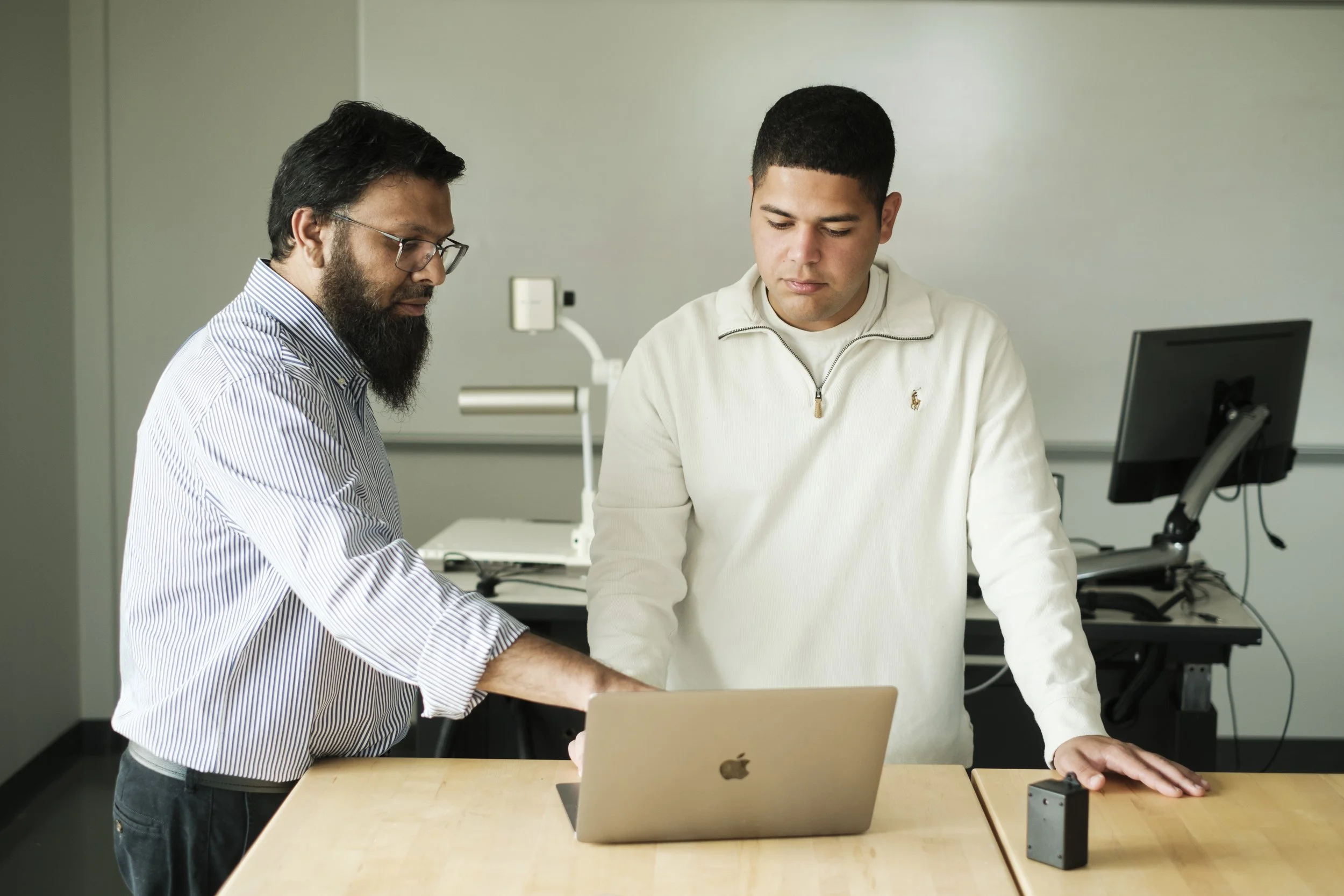 Two men look at a laptop on a table.