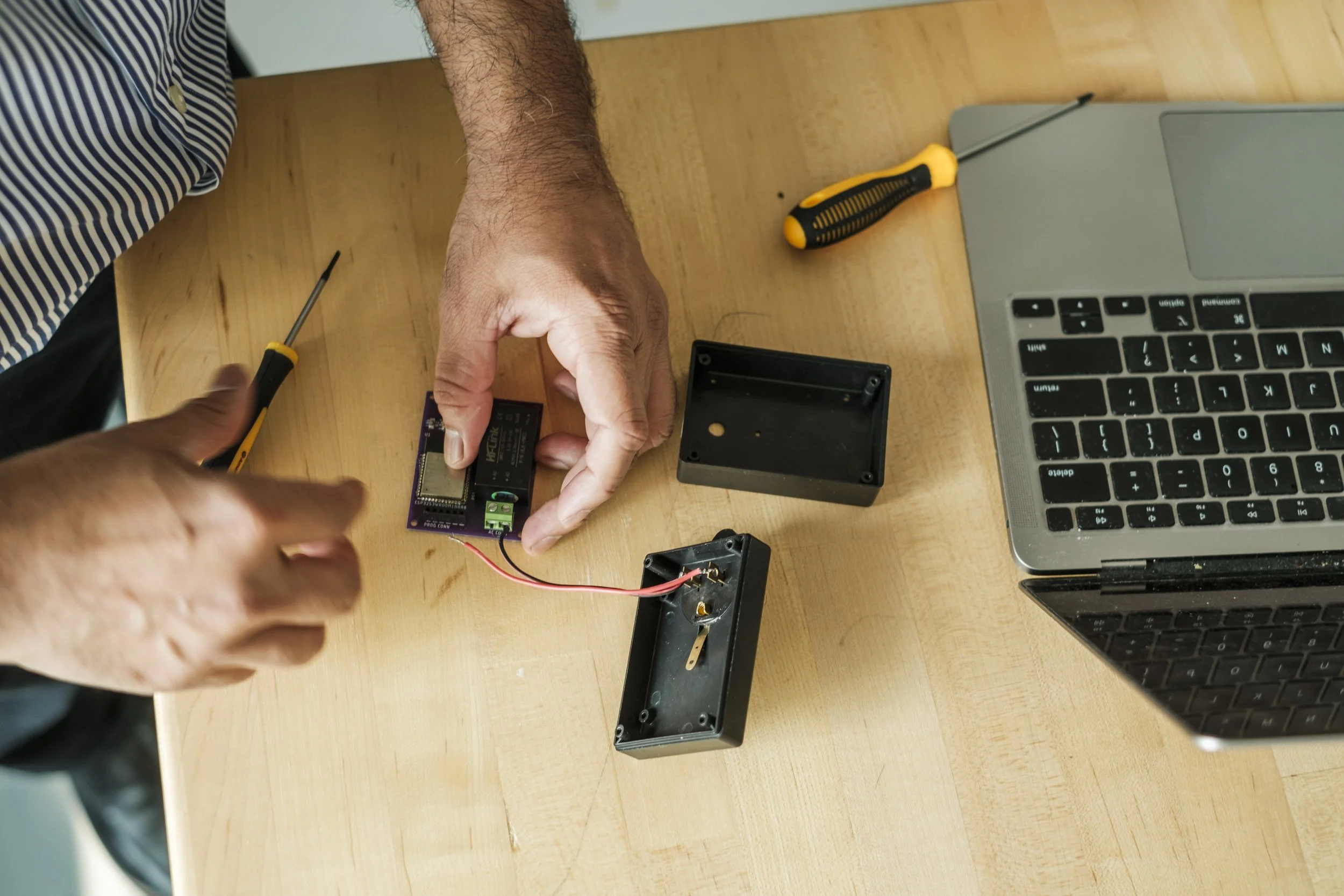 Hands assembling a device on a table with red wires exposed..