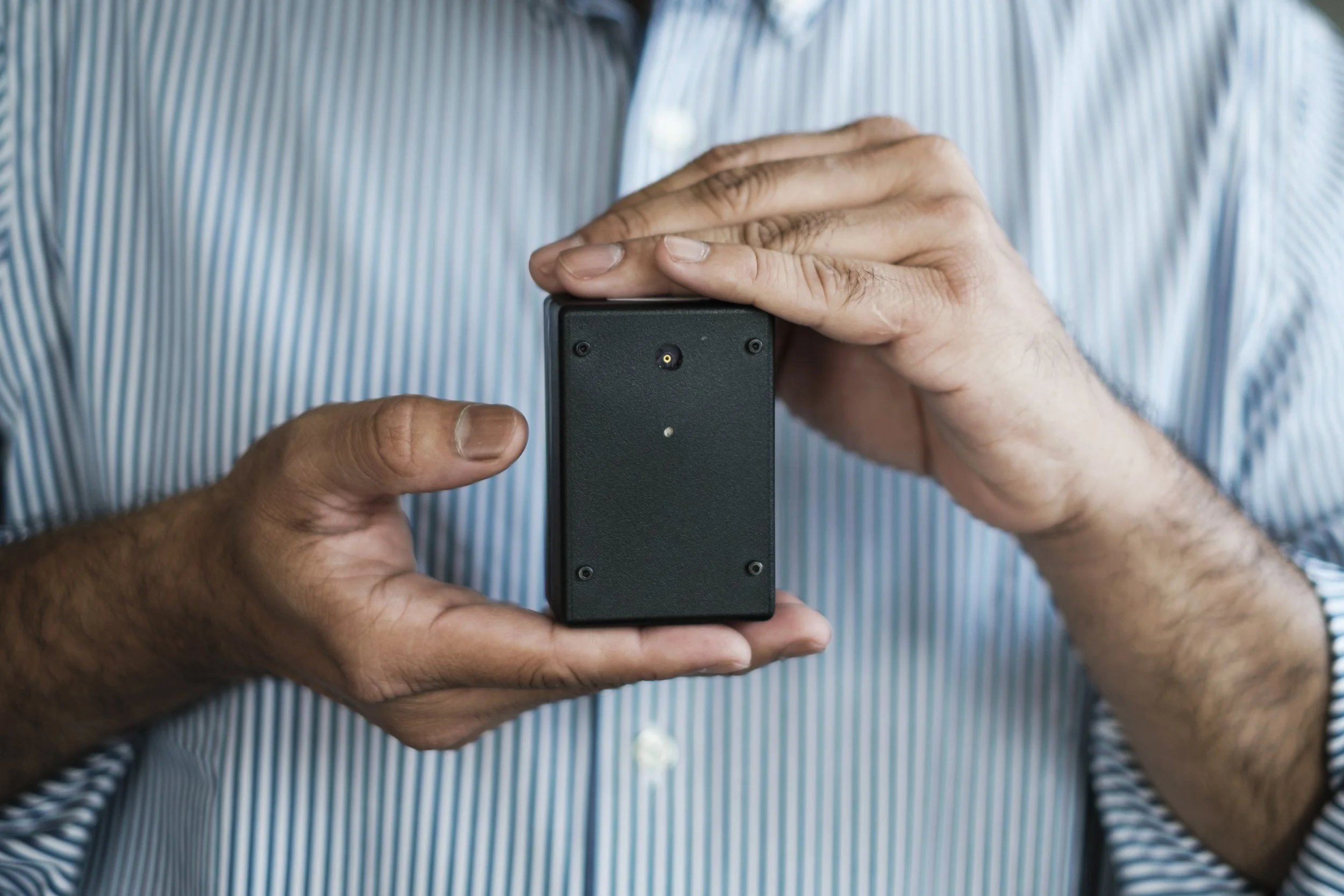 Hands hold a small black electronic device.