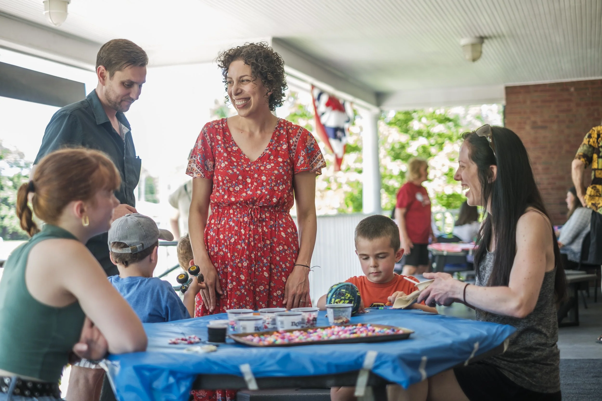 A group of people stand on a porch of a library, smiling at each other, with children in the foreground.