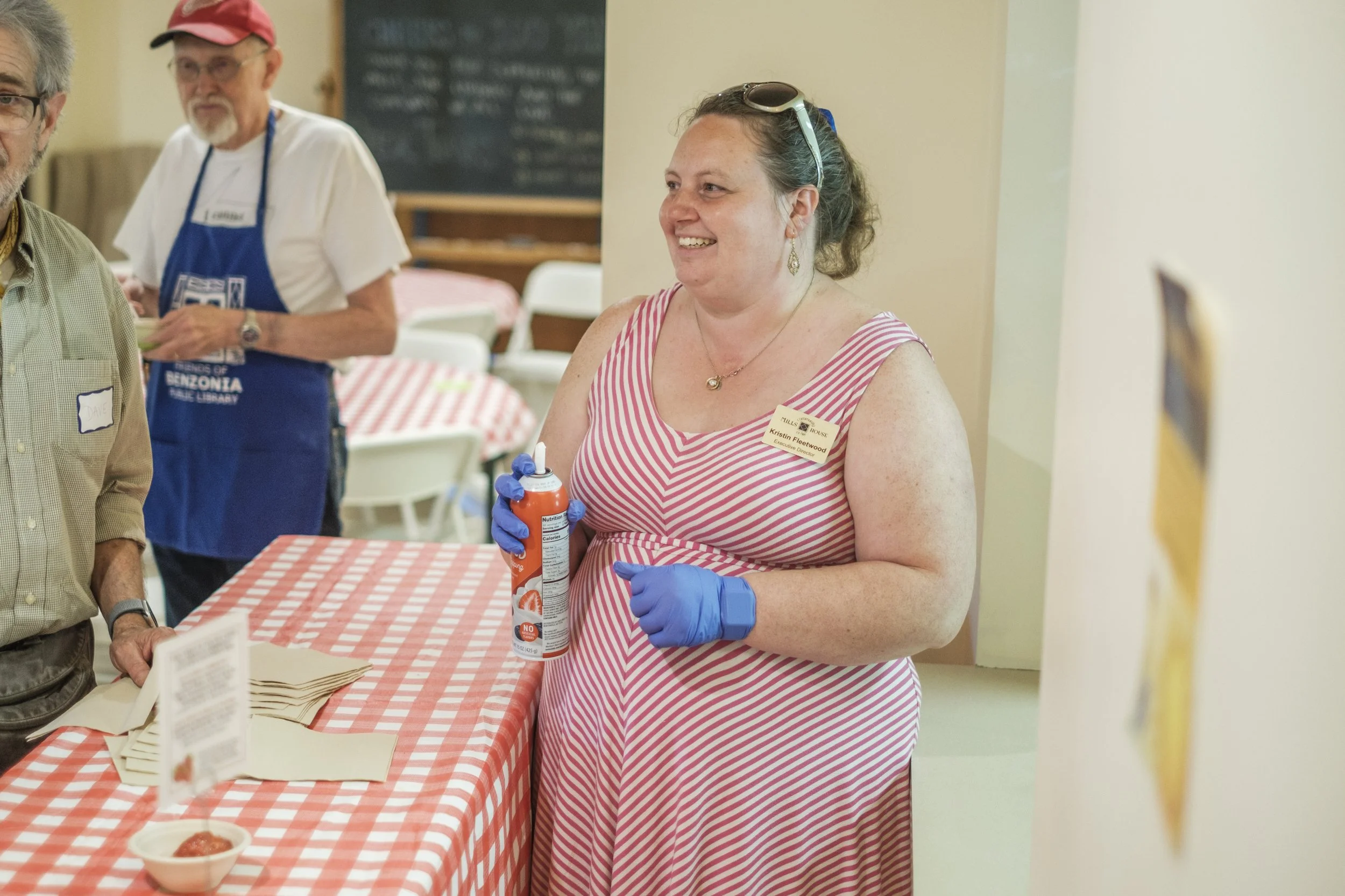 A woman stands holding a can of whipping cream and smiles behind a table.