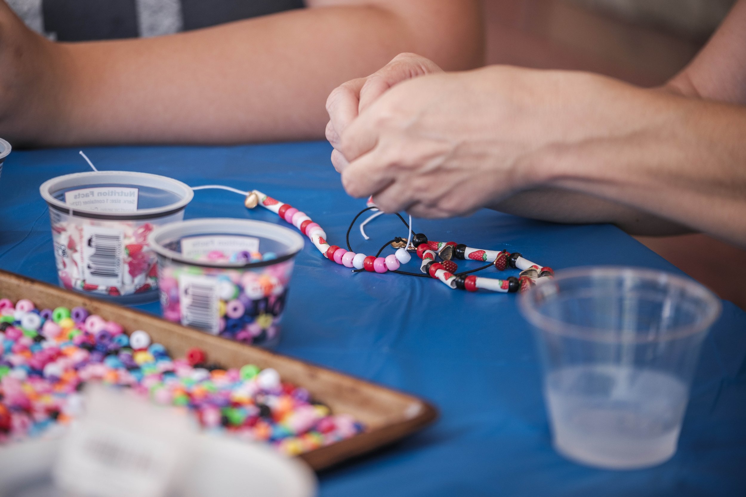 Hands tie a piece of string with beads on it while it sits on a blue table.
