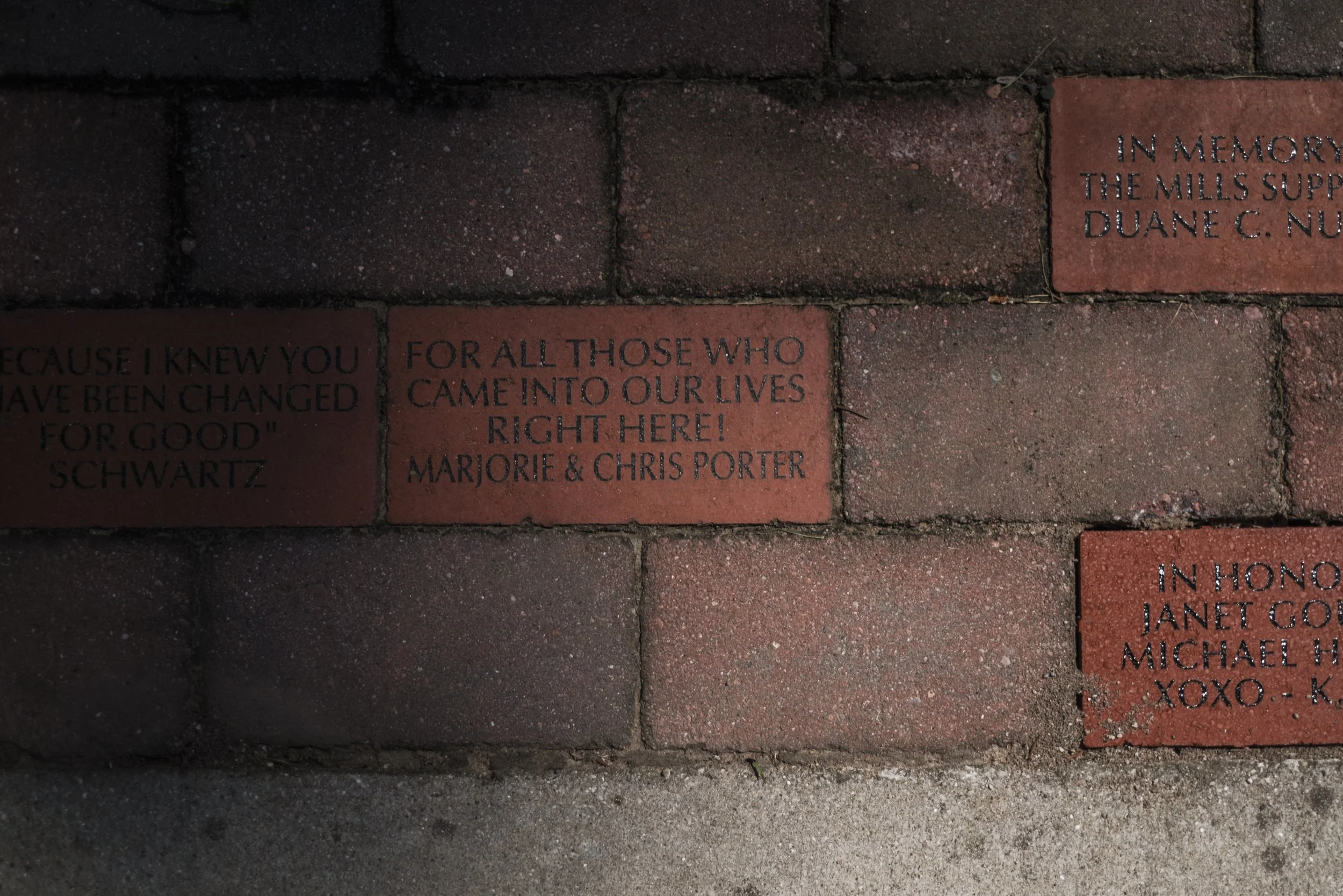 A brick in pavement that reads "for all those who came into our lives right here! marjorie and chris porter".