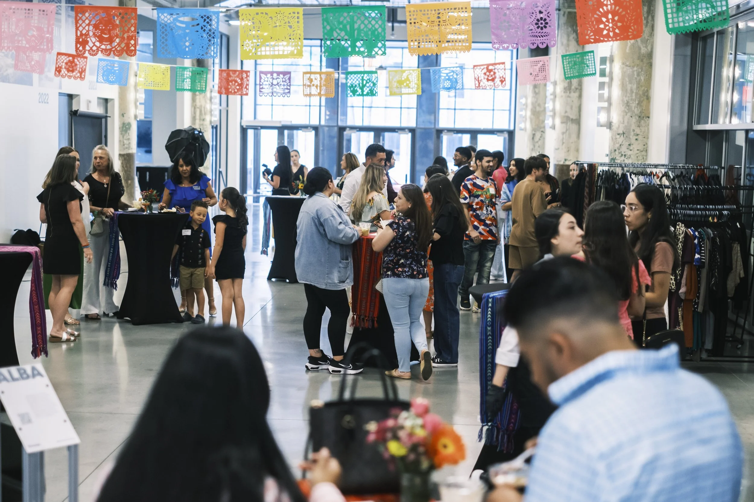Attendees at MiHC’s Gran Fiesta, stand at tables with colorful paper decorations overhead.