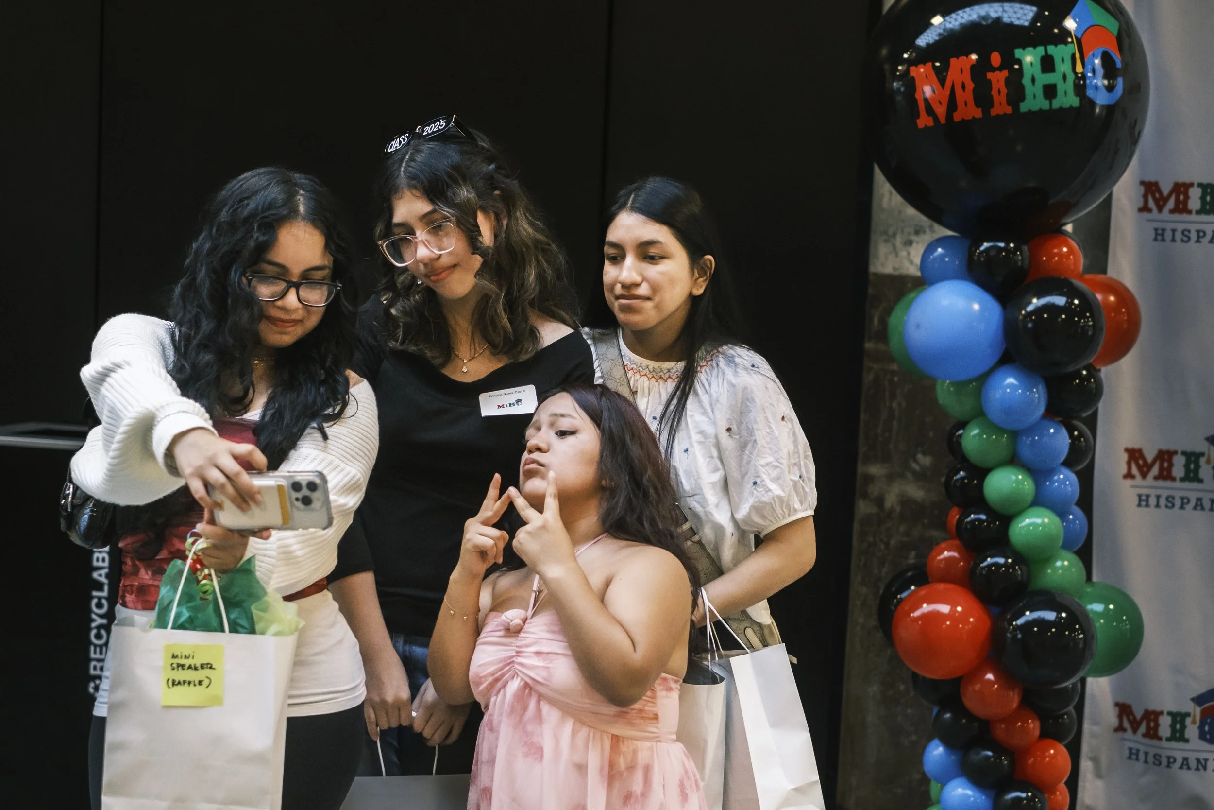 Four young women pose for a selfie with a cell phone in front of a stand and repeat.