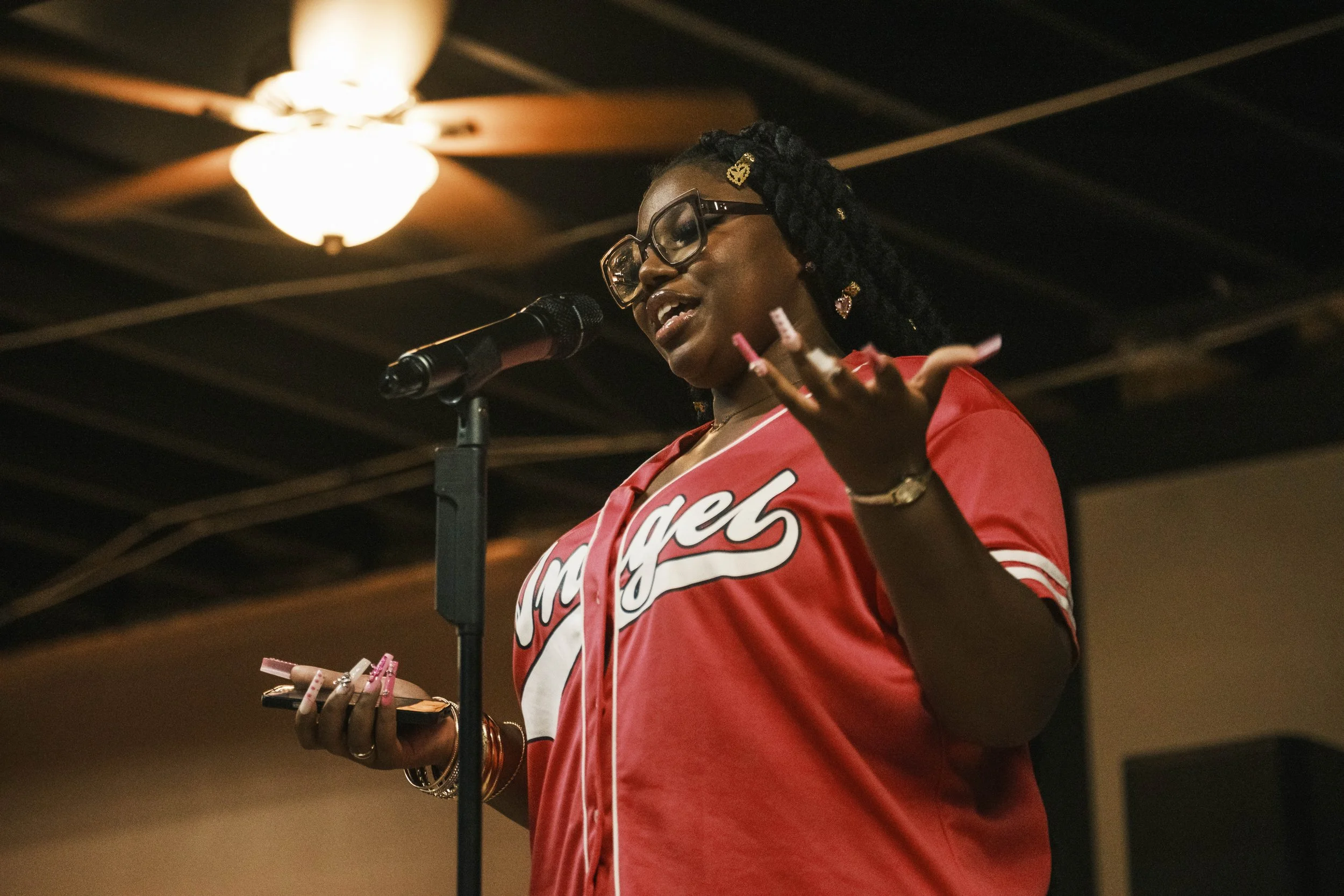 A poet onstage at wearing a pink jersey during an open mic poetry event in Detroit