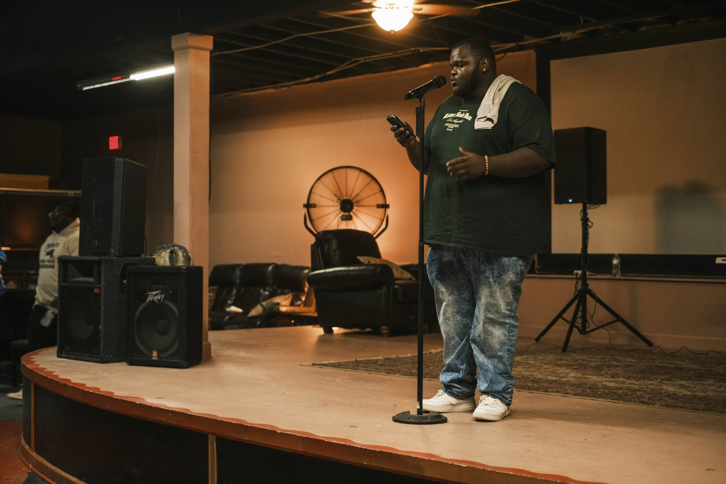 SolFull Poetry reads from their phone on stage during an Open Mic poetry event at Artist Village in Detroit