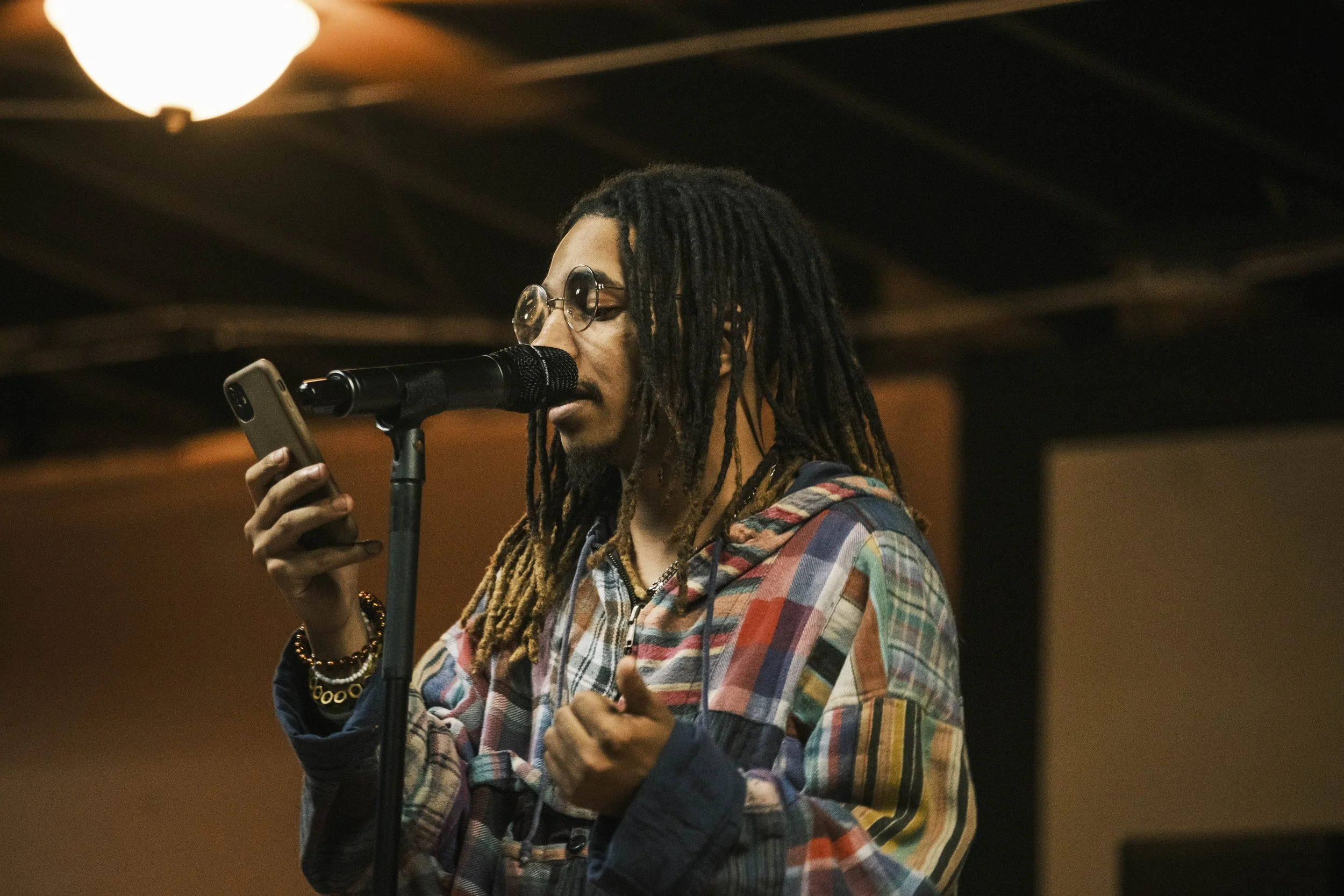 A poet reads from their phone on stage during an Open Mic poetry event at Artist Village in Detroit