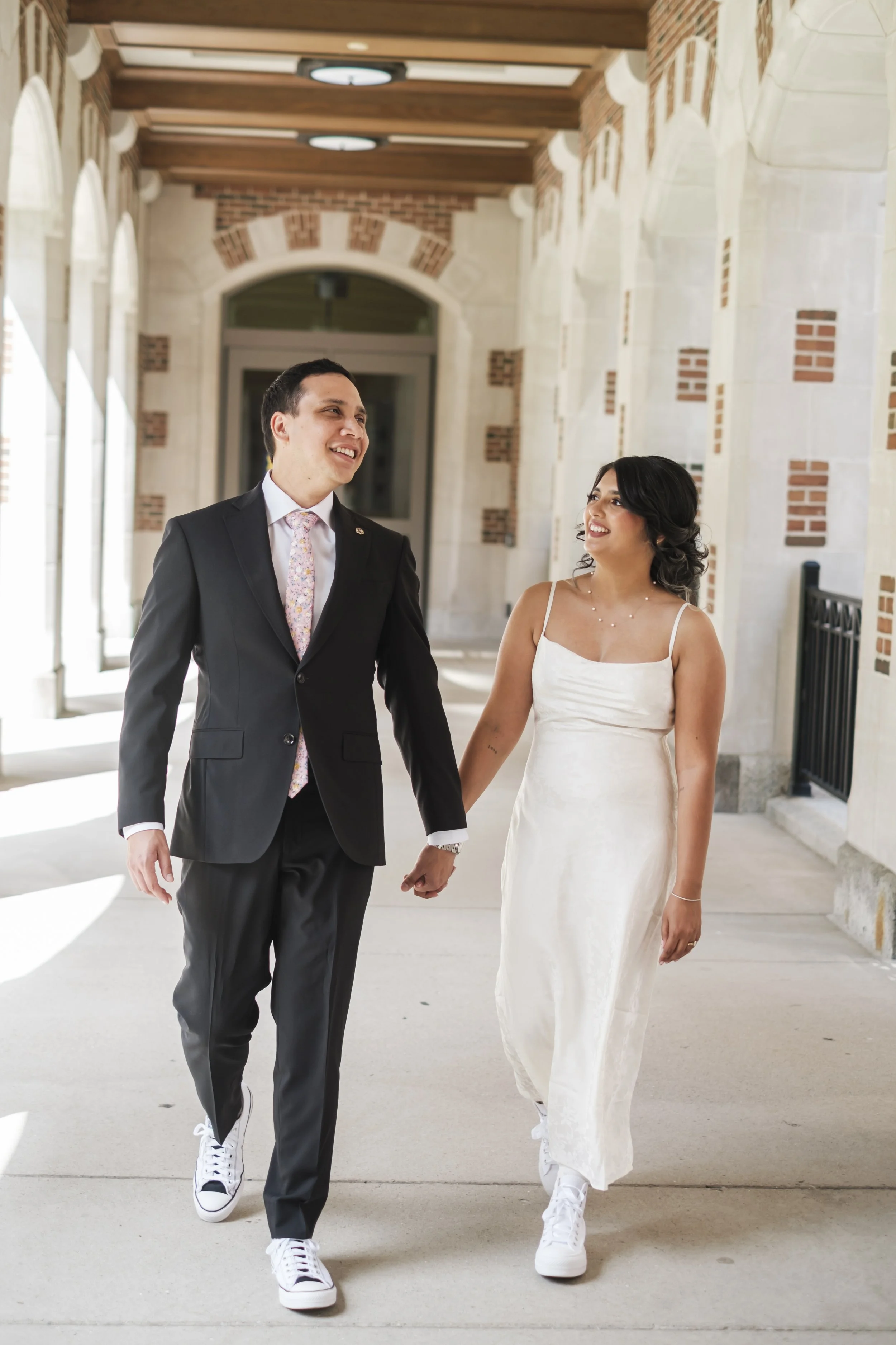 A bride and groom walk between brick pillars.