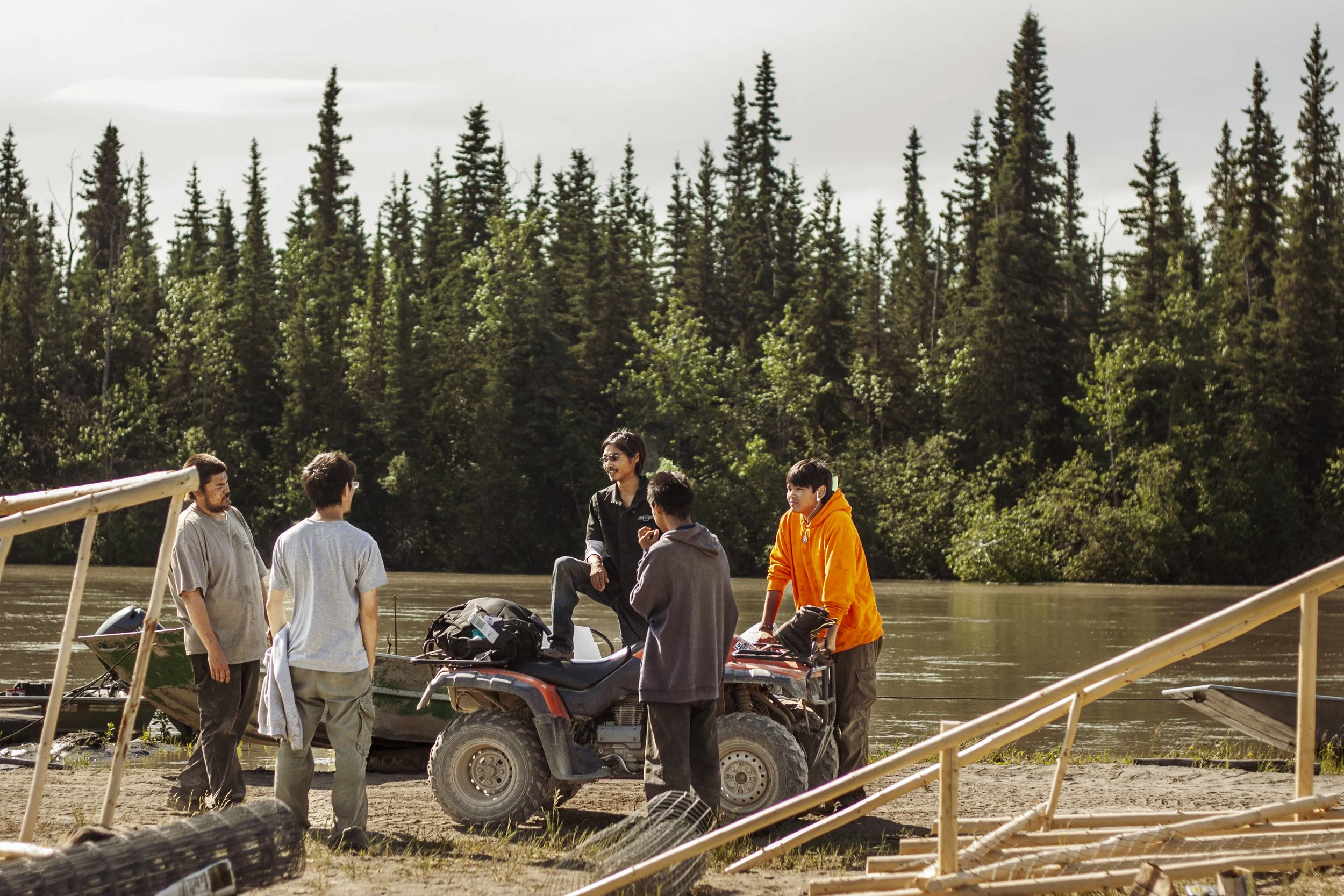 A group of young people talking around a Four Wheeler in a remote part of Alaska, surrounded by trees.