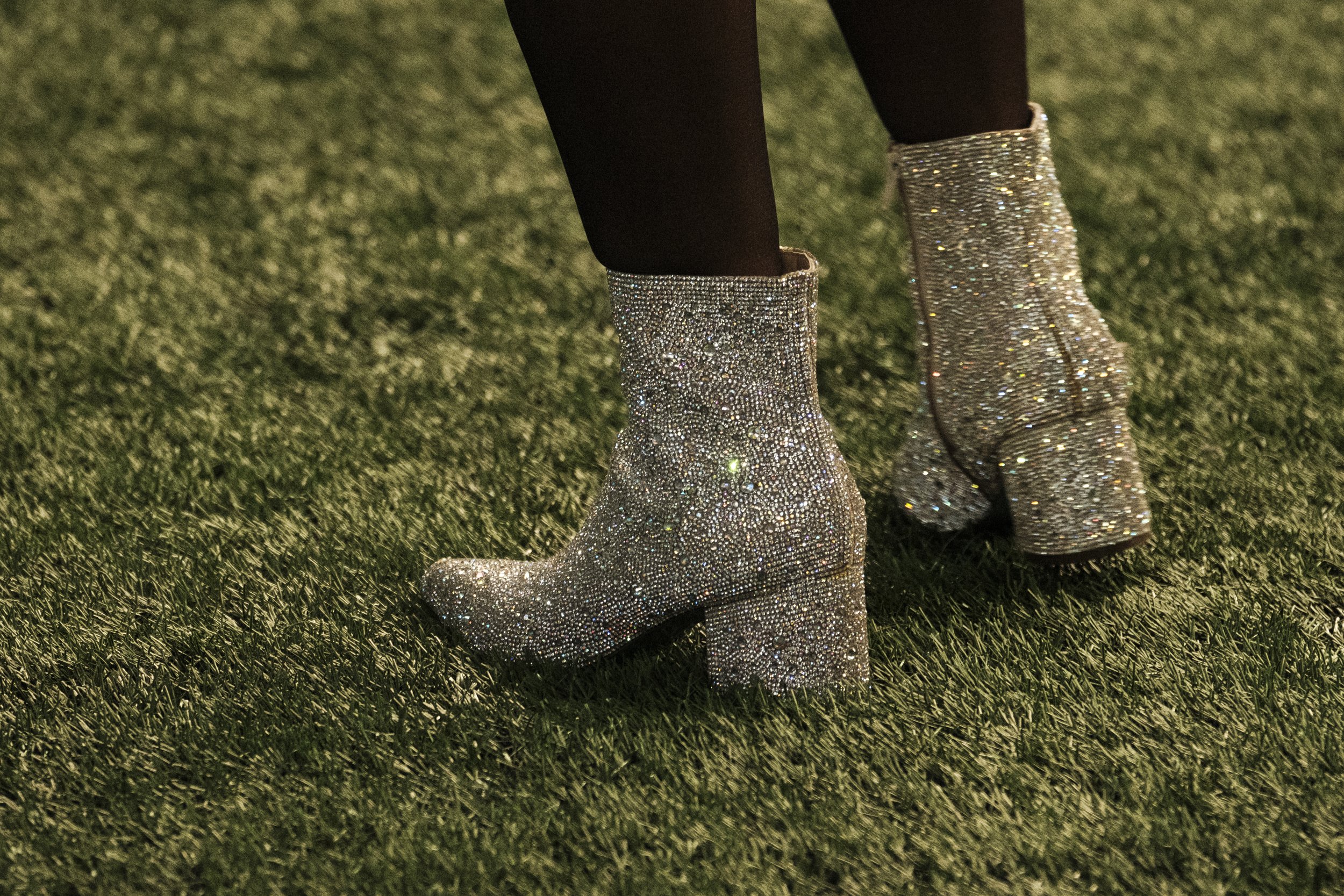 A close up of sparkly, silver boots standing on turf.