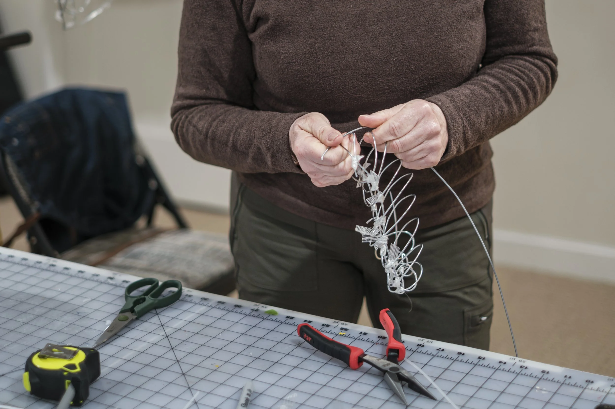 Hands bend and weave loops of metal wire.