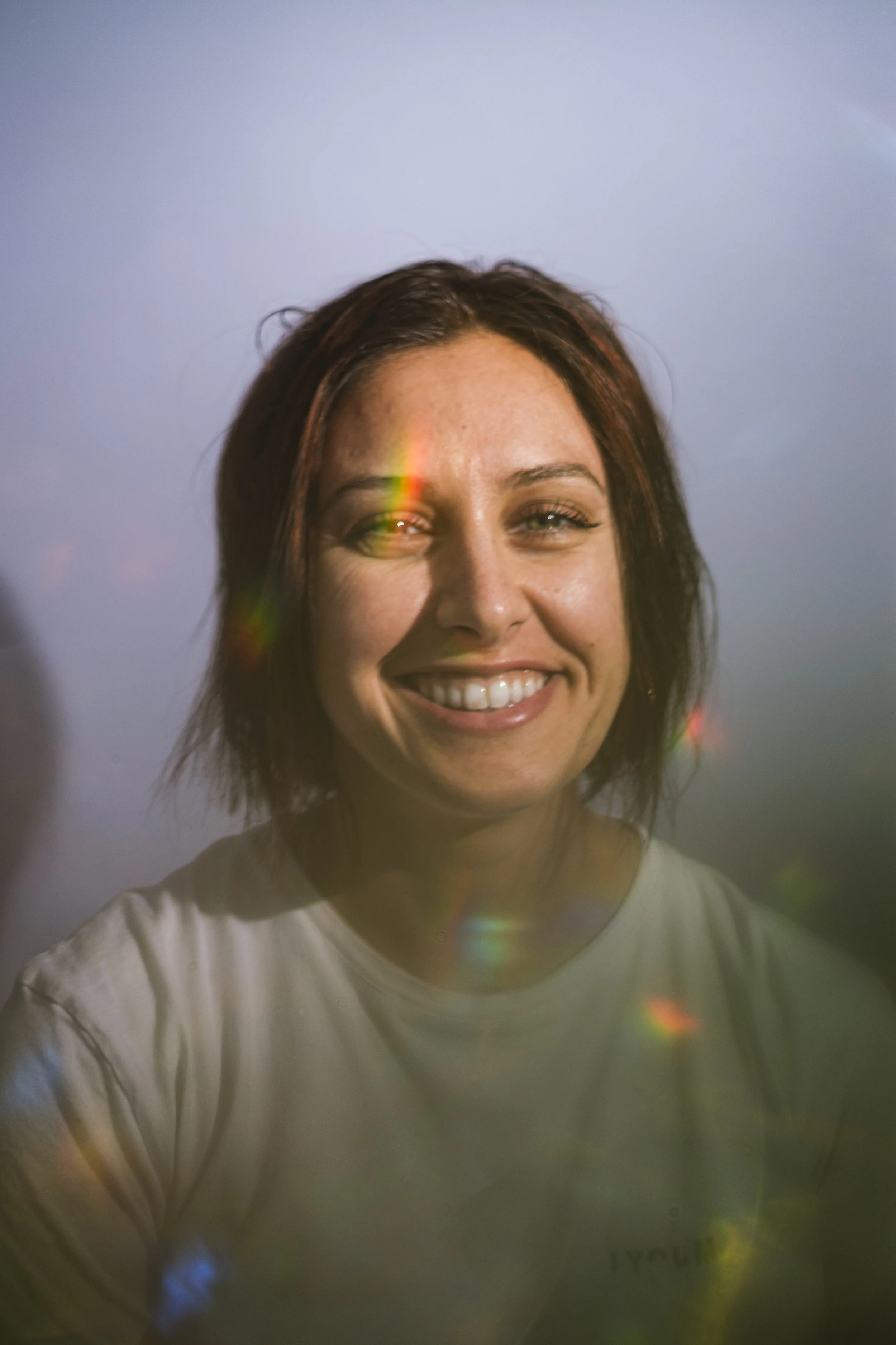 A photo of a young woman smiling against a gray backdrop with rainbows in the foreground.