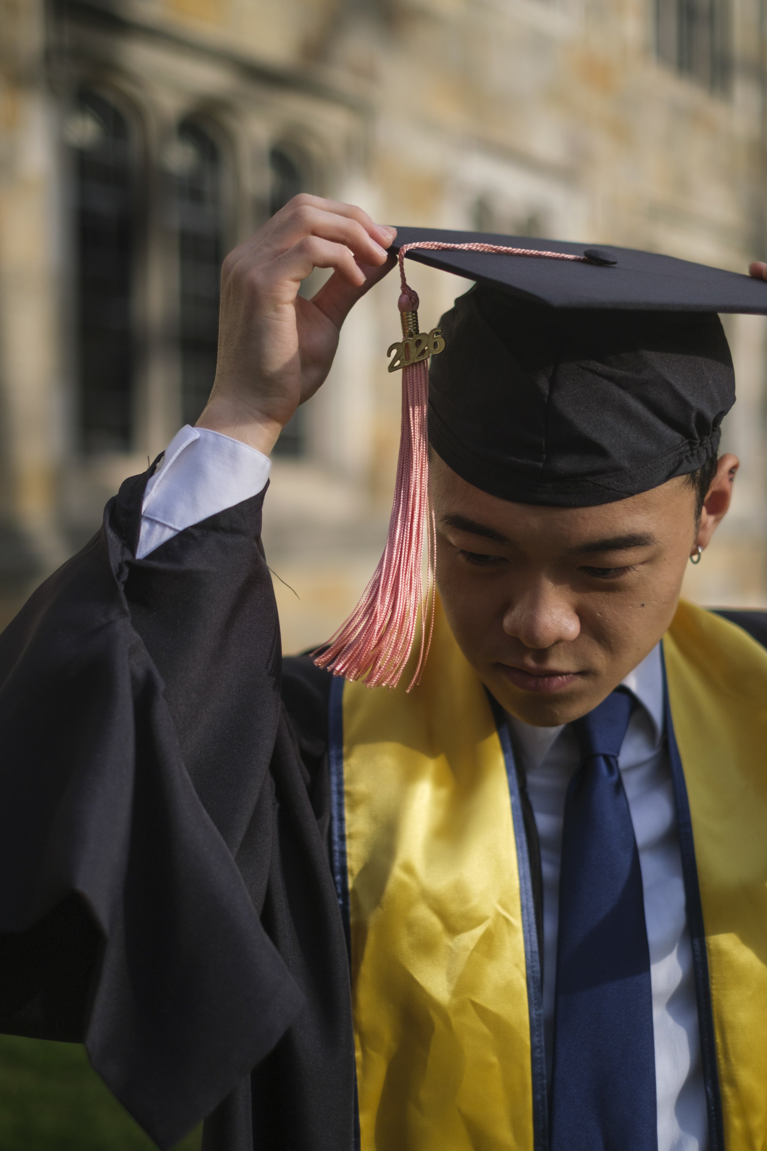 A person adjusts their graduation cap while an attached tassels blows in the wind.