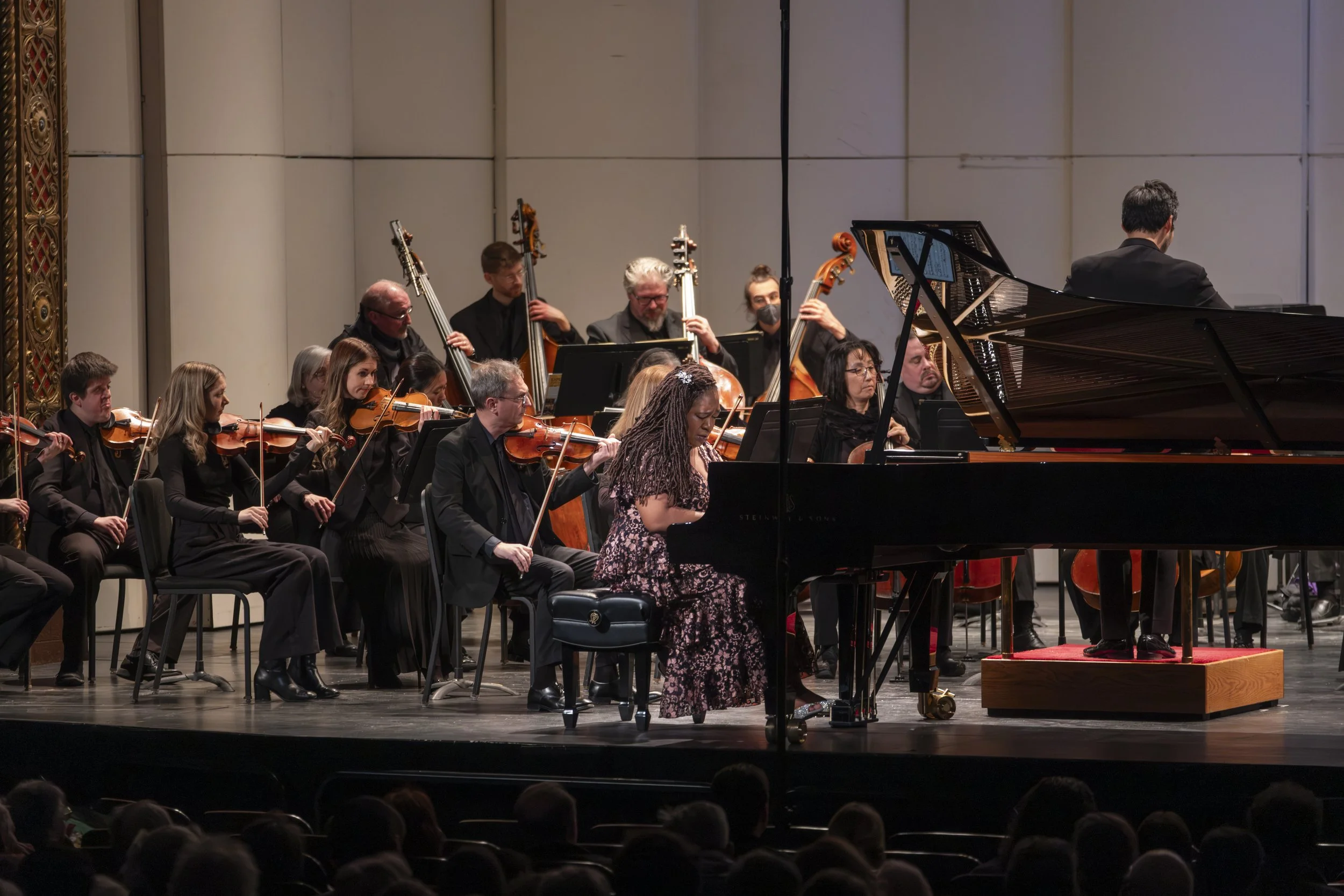 Pianist Michelle Cann plays a grand piano on stage while an orchestra plays behind her.