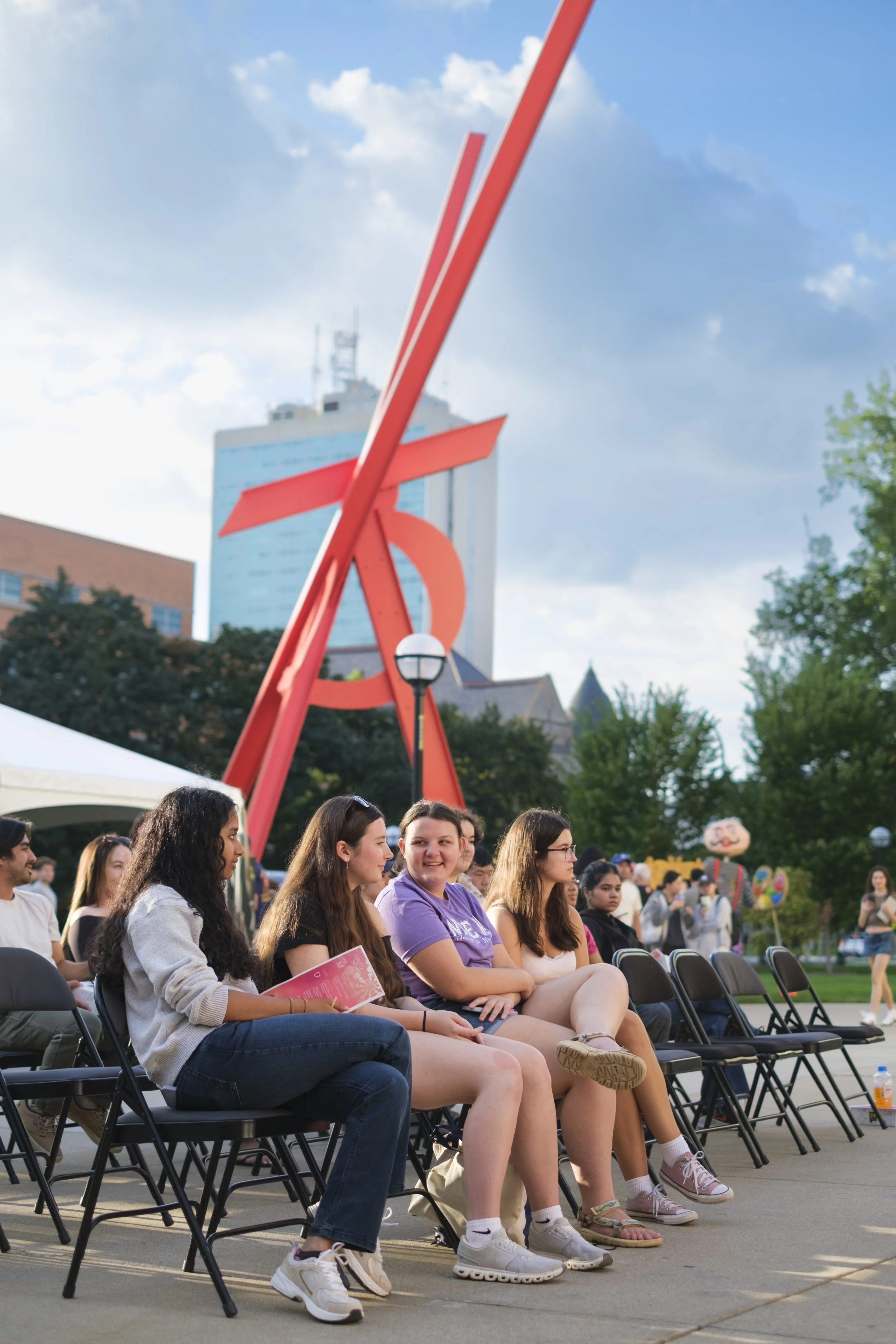 A group of people in the audience of Artscapade smile at one another while the scultpure Orion is in the background.
