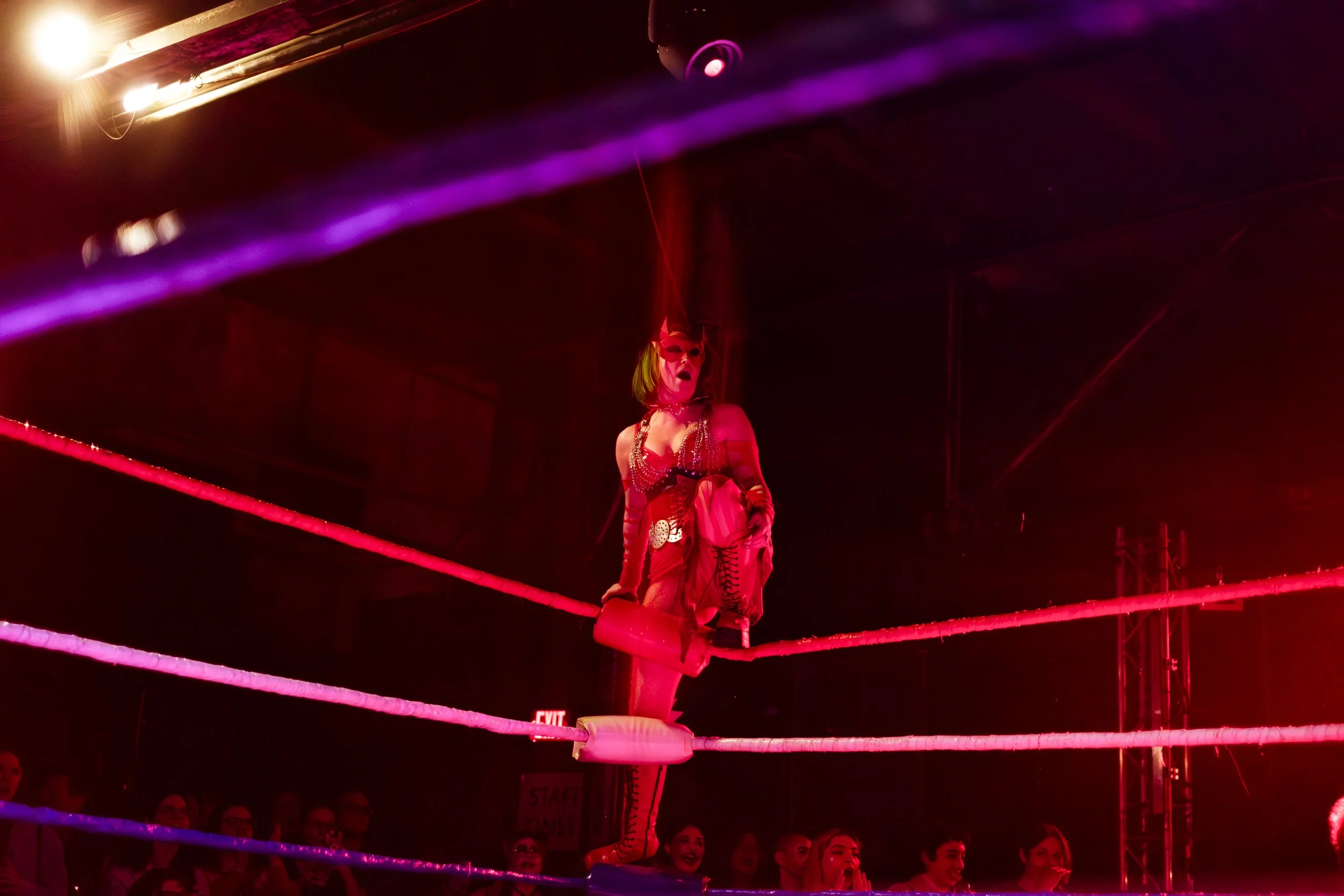 A wrestler known as the Red Witch, stands at the edge of a wrestling ring while yellow out at the audience.