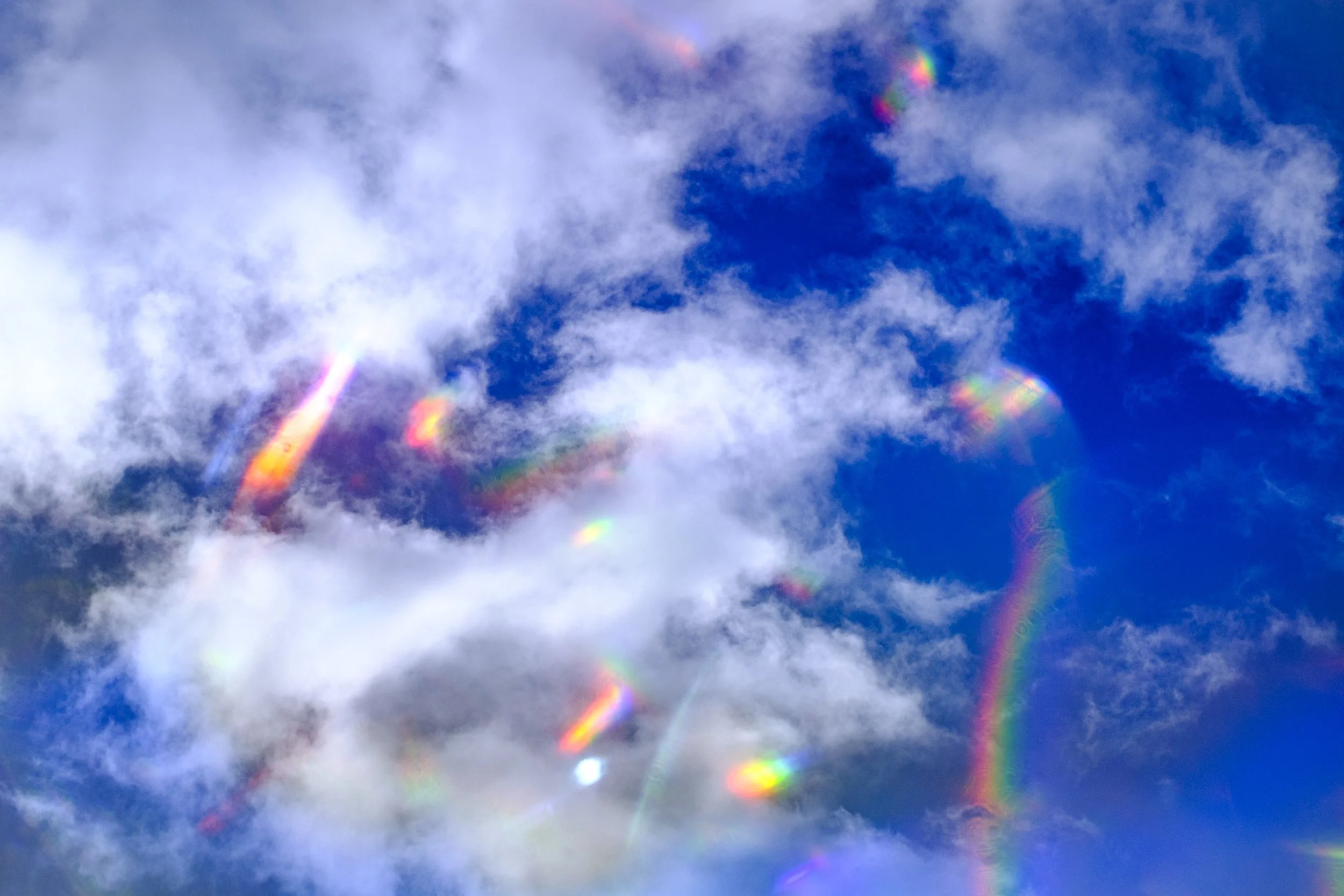 White clouds against a blue sky with small rainbows.