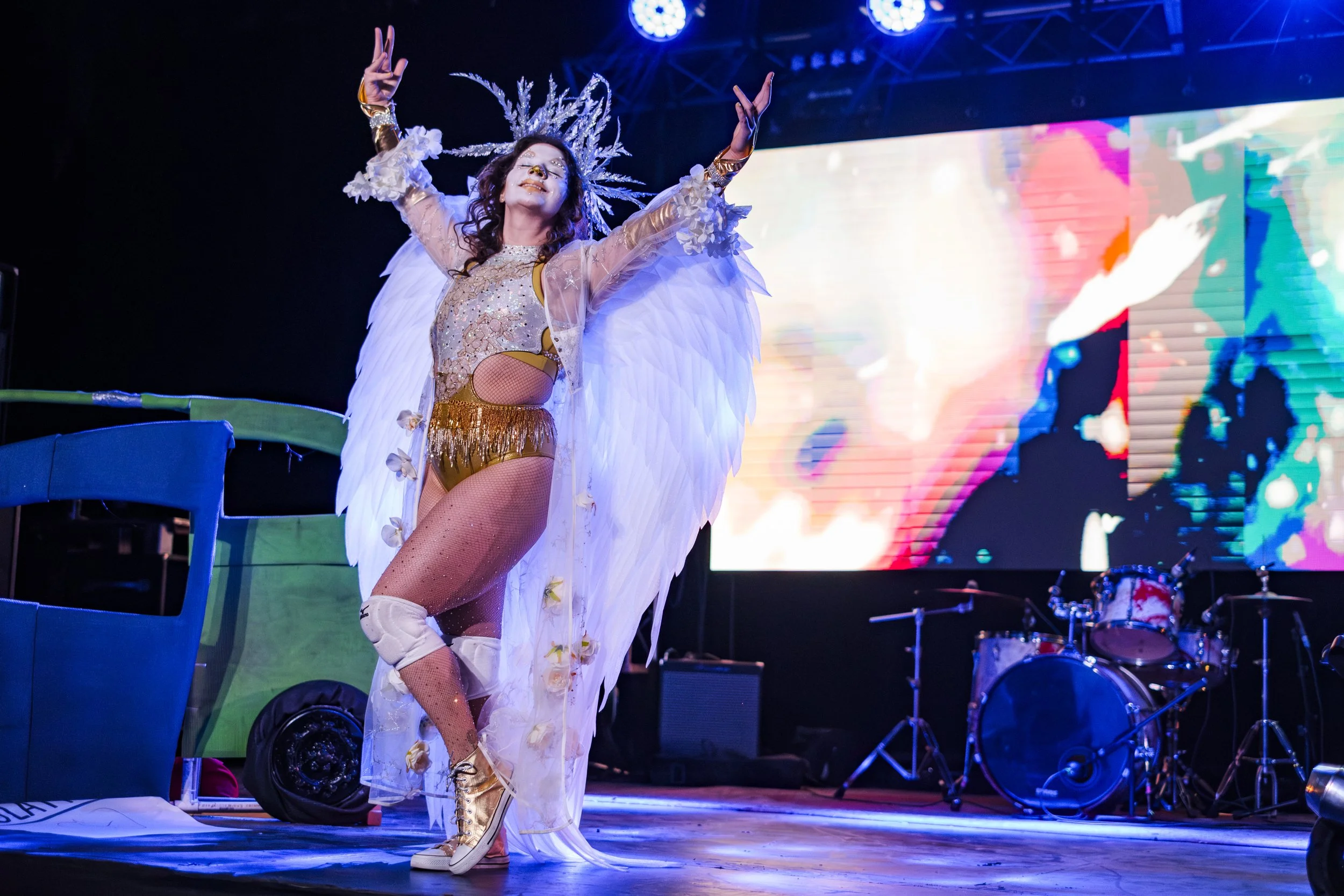 Clown wrestler Bella Benevolence walks out during her entrance, holding her hands over her head, wearing angel wings, on-stage.