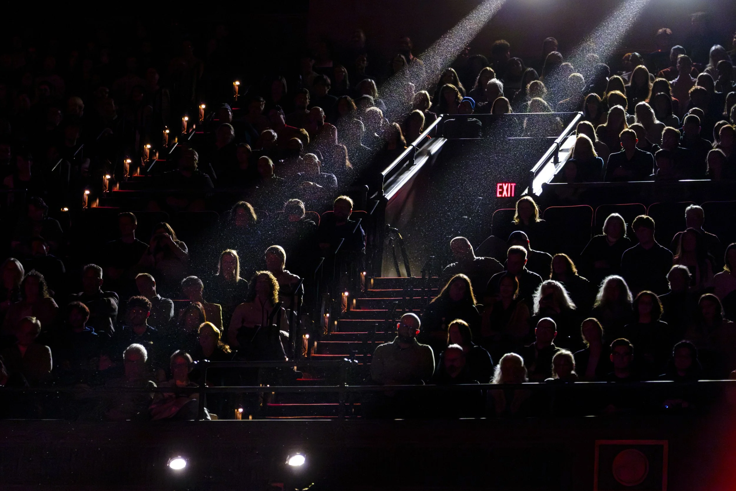 A group of people sit in theater seating are backlit by stage lighting in an auditorium.