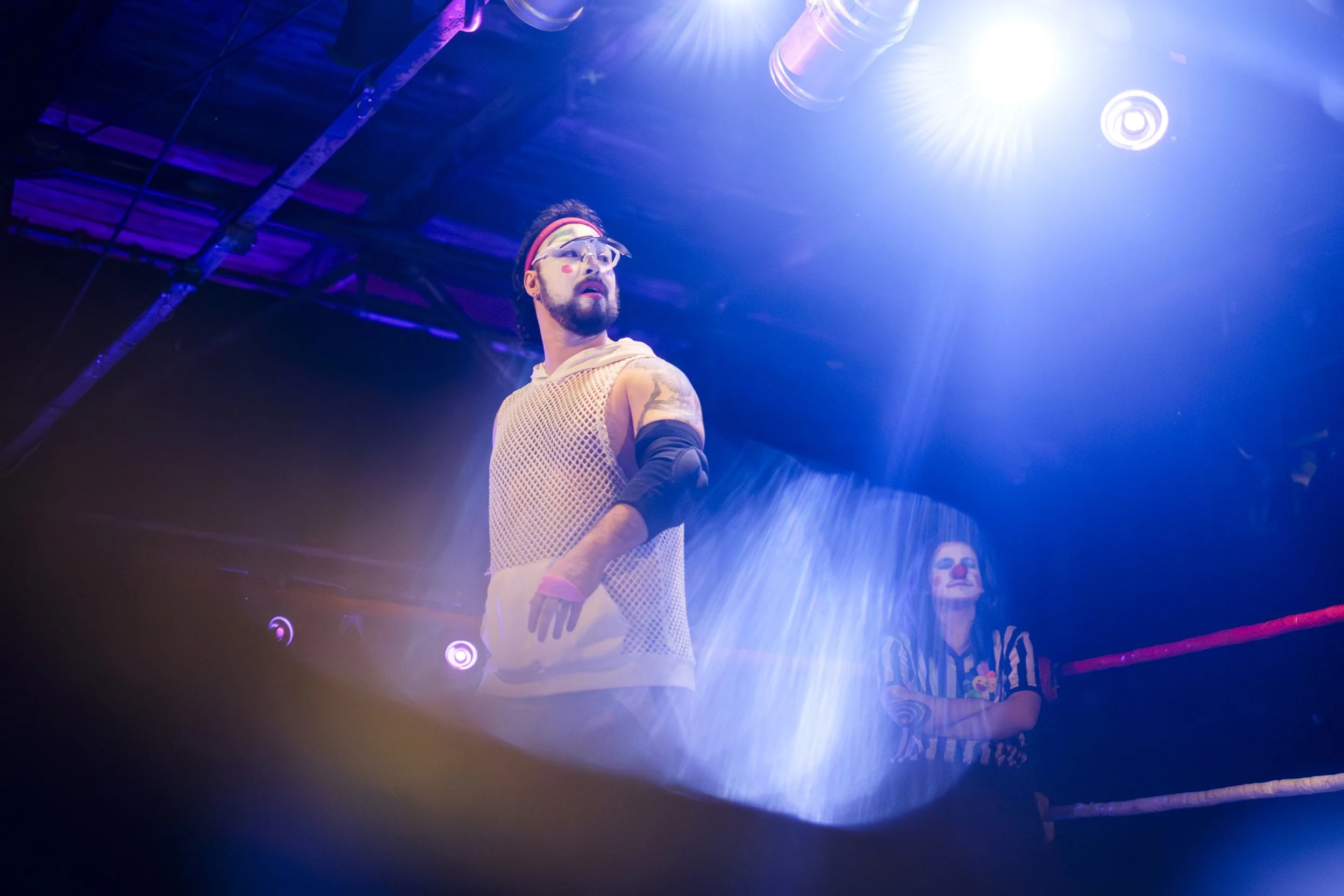 Clown wrestler Tom-E Forklifts looks at his opponent while standing in a wrestling ring.