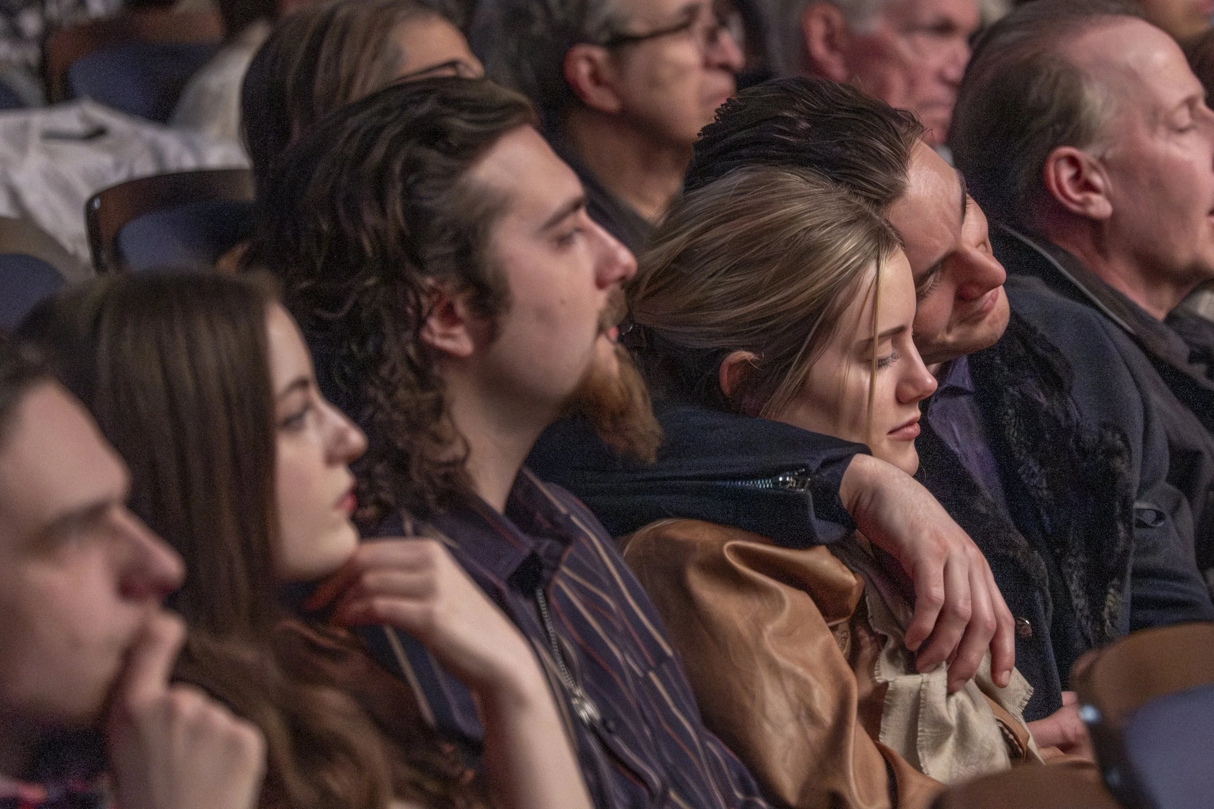 Audience members listen with their eyes closed and arms around one another.