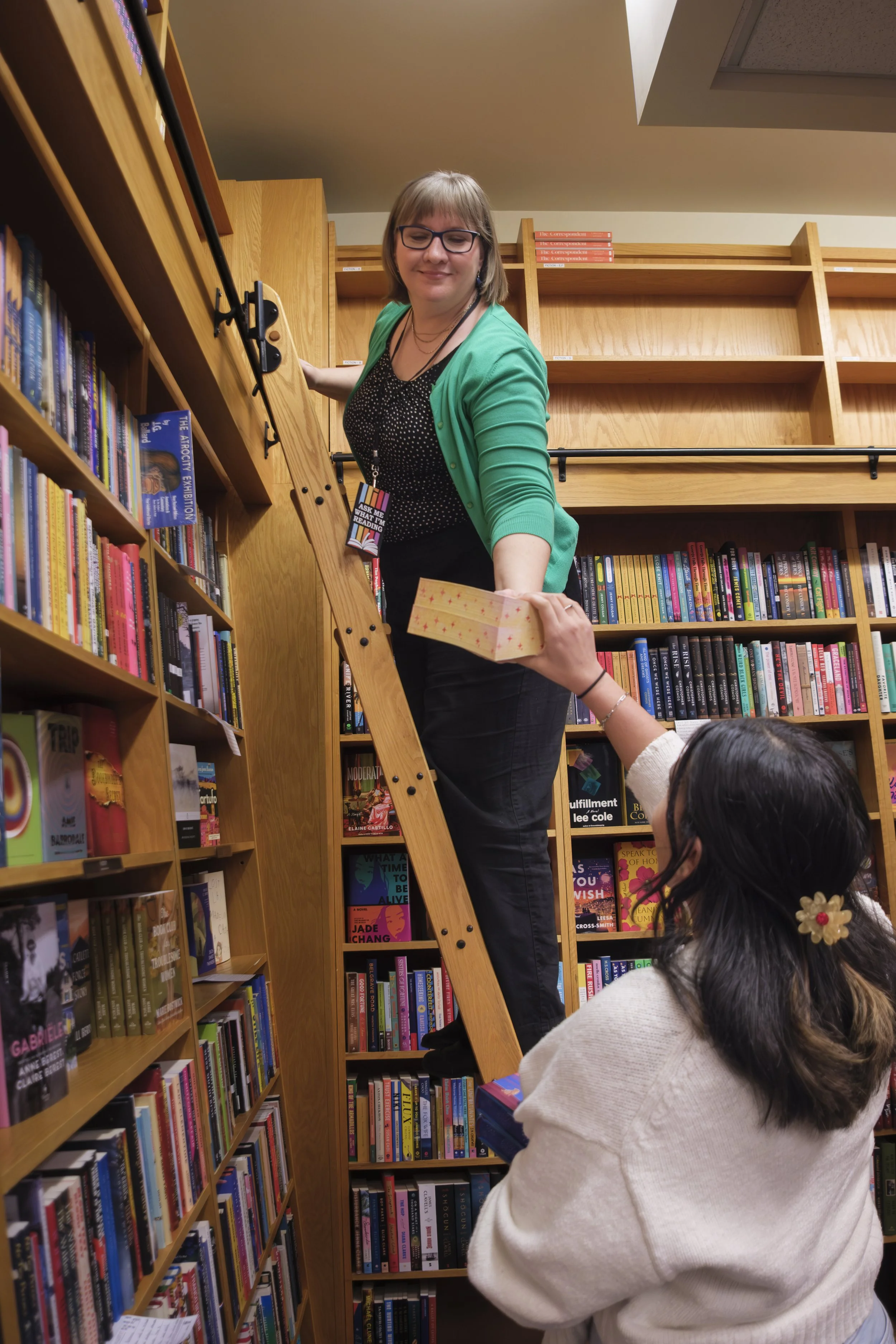 An employee smiles while standing on a ladder and taking books from another employee at the Schuler Books in Grand Rapids, Michigan.