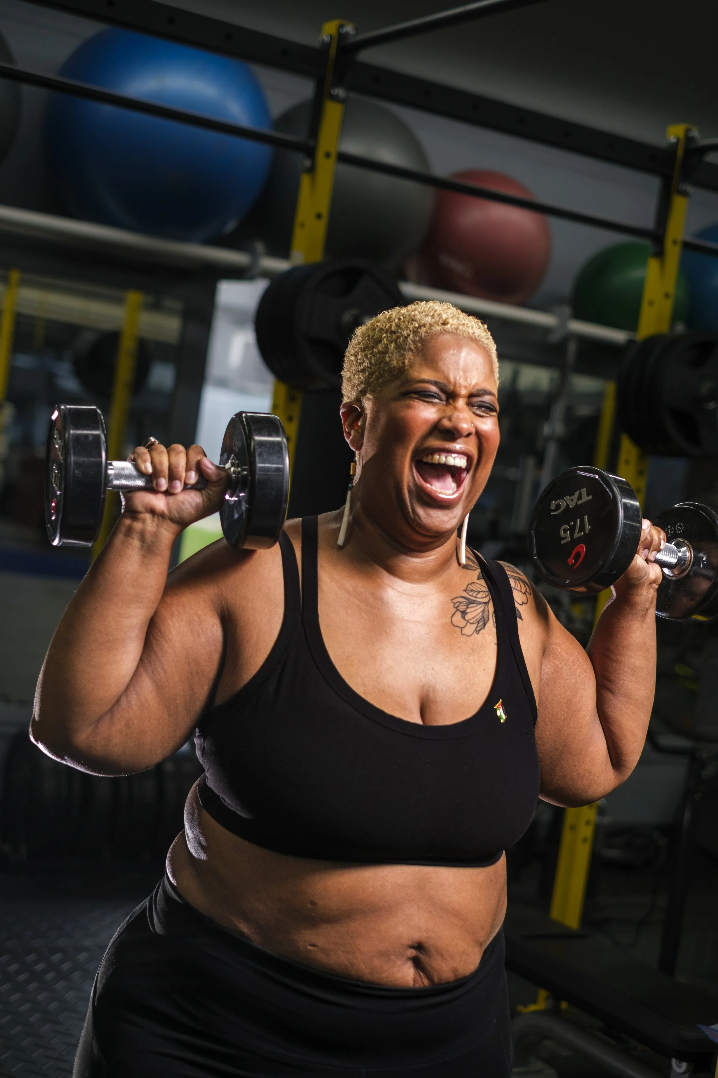 A woman shouts while lifting up dumbells during a work out session at a gym.