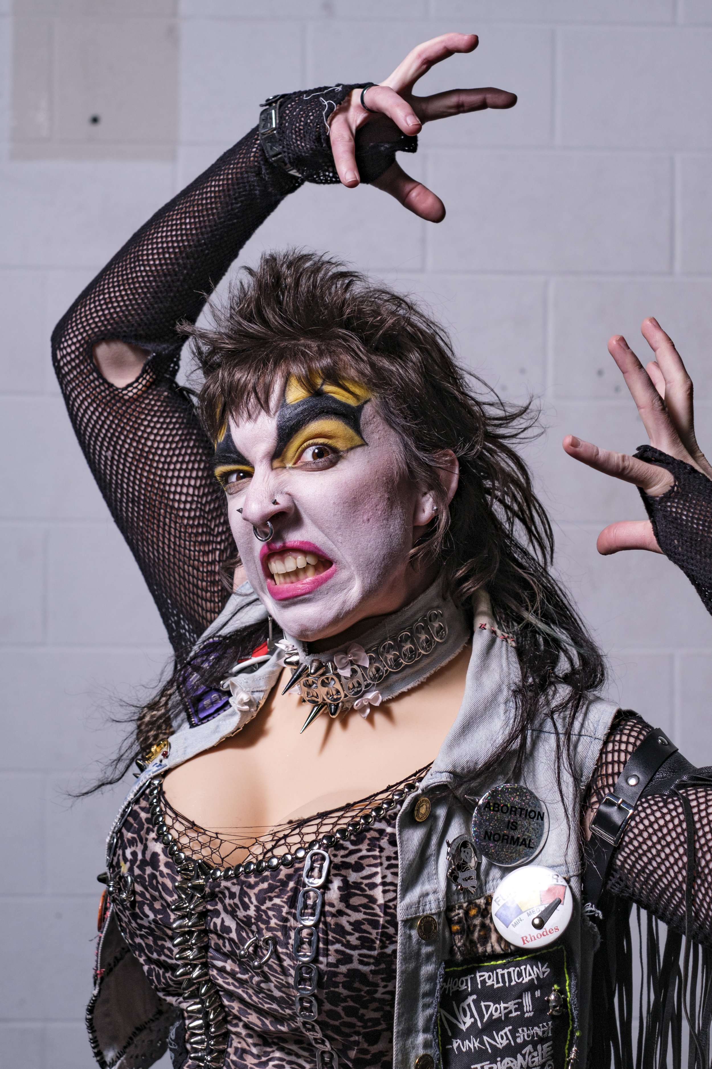 A person snarls at the camera while wearing clown makeup and bright yellow eye shadow.