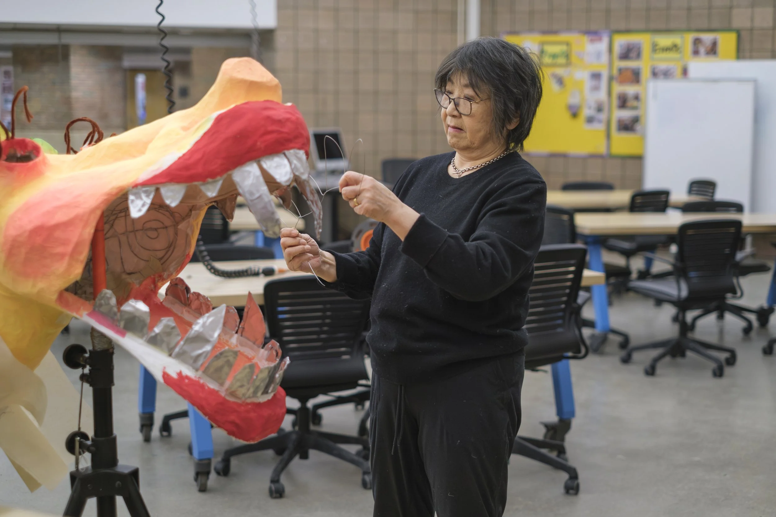 Artist Zhen Guo holds up metal wire next to a dragon head art piece.