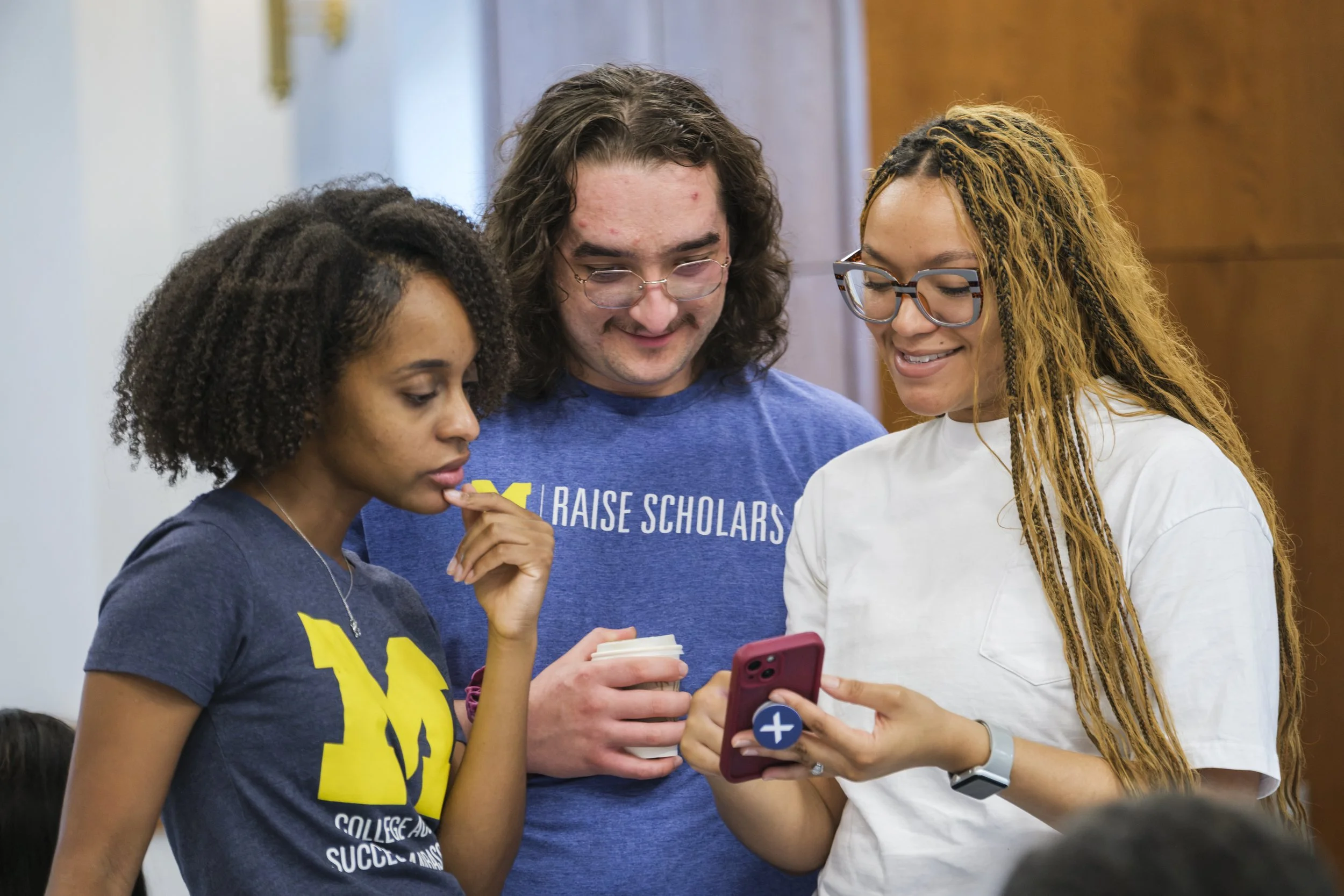 Three people, who work for the Center for Education Outreach at the University of Michigan look at one phone while standing.