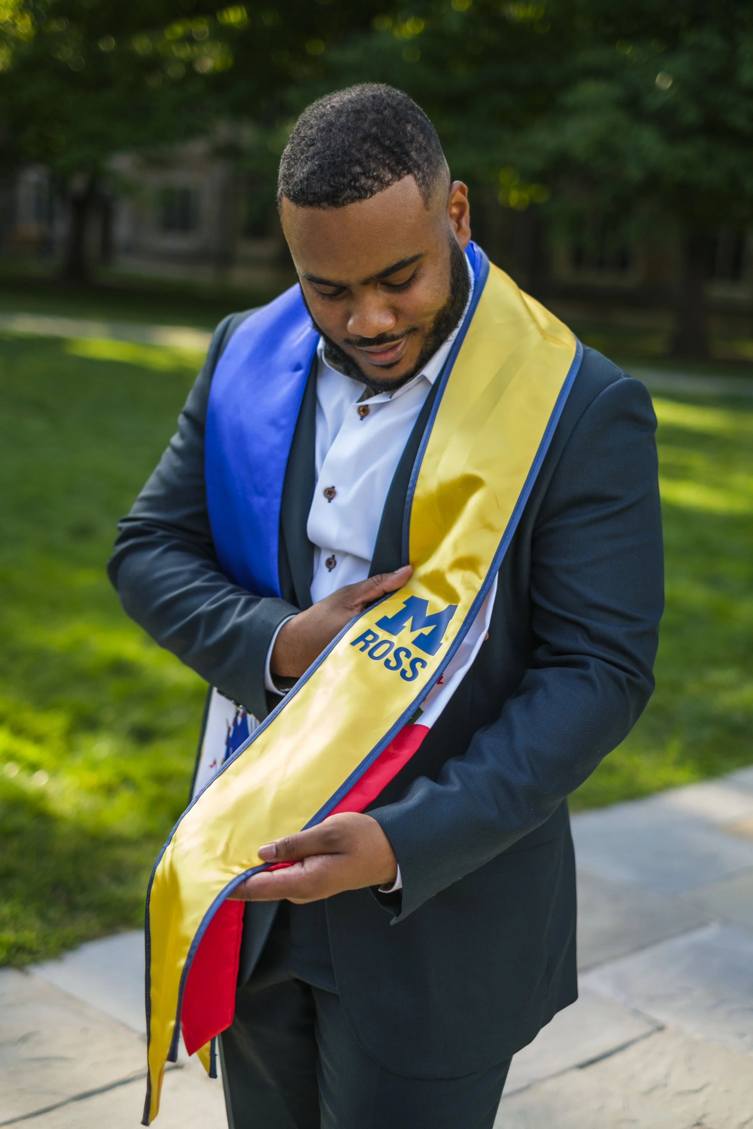 A man holds his graduation stole that reads "Ross" with the University of Michigan Block M.