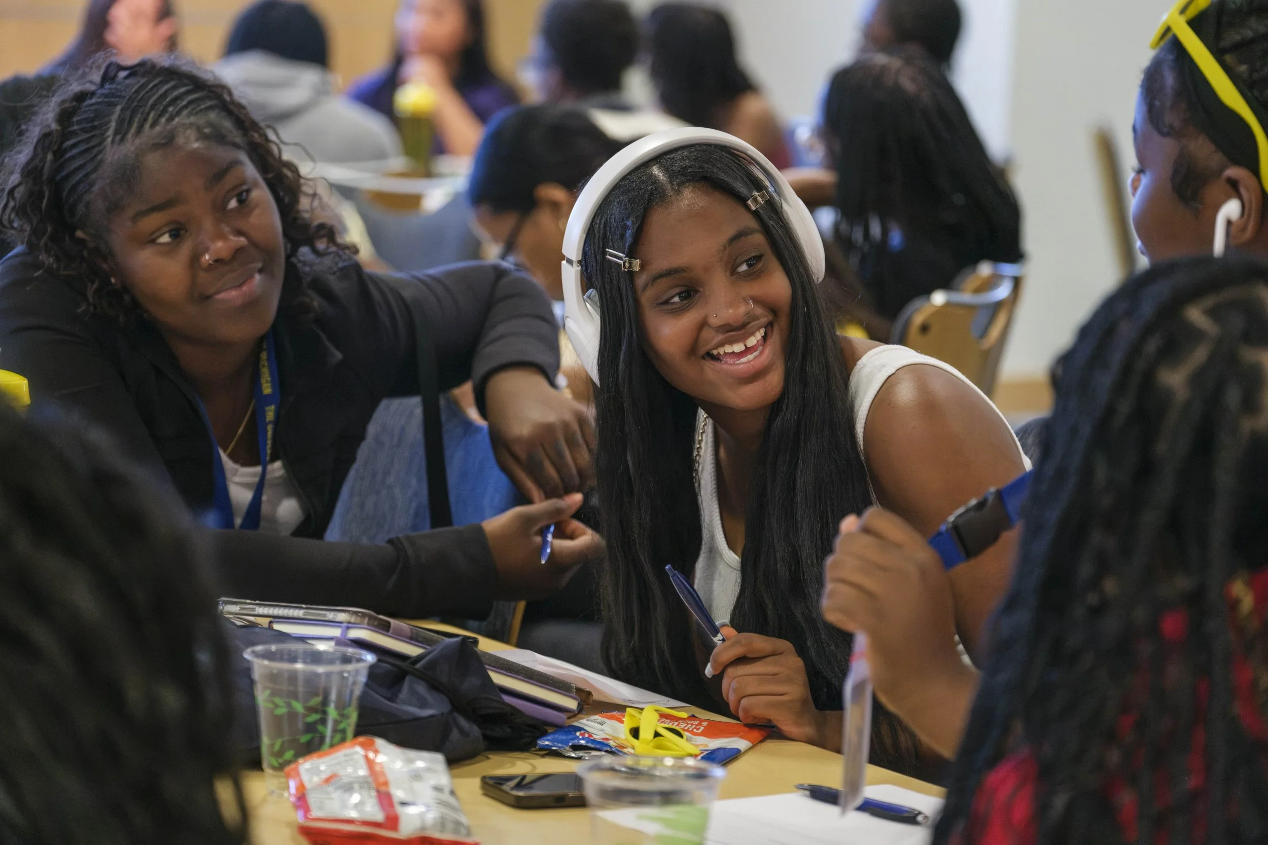 High School students smile and talk with one another while sitting at a table with snacks scattered on top.