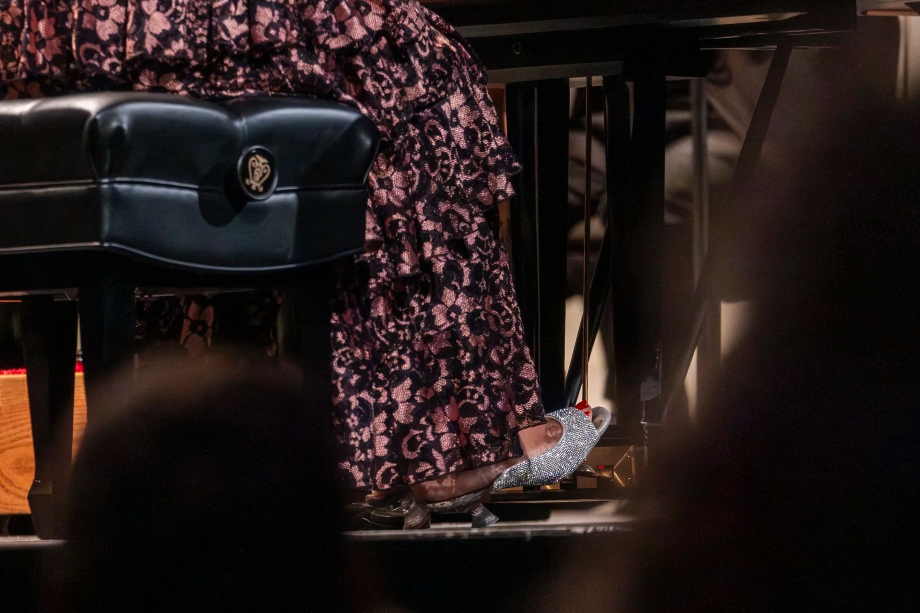 A foot wearing a shiny heeled shoe presses on a piano peddle.
