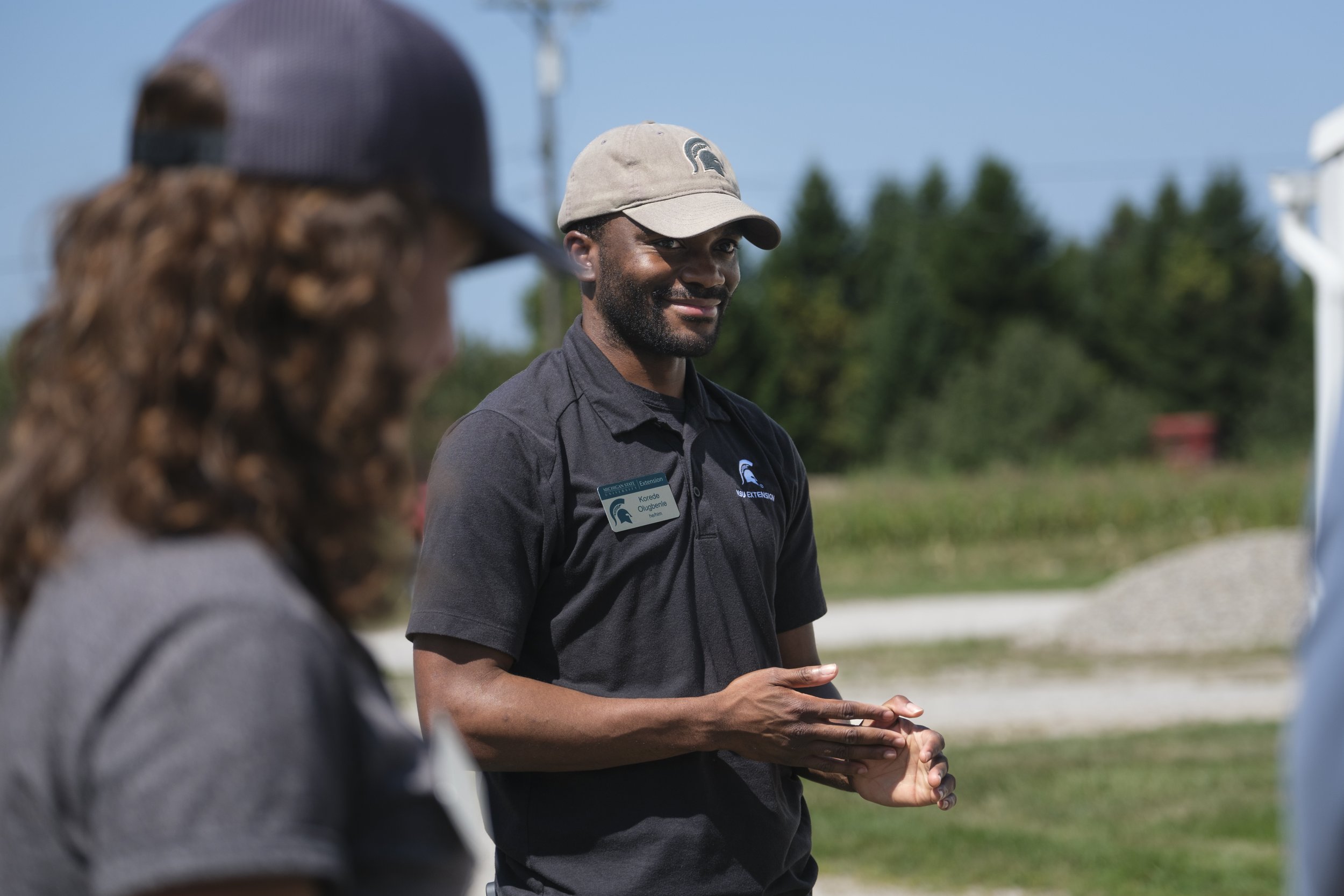 A man wearing a Michigan State University polo and baseball hat stands next to a woman during a rainfall simulator device demonstration.