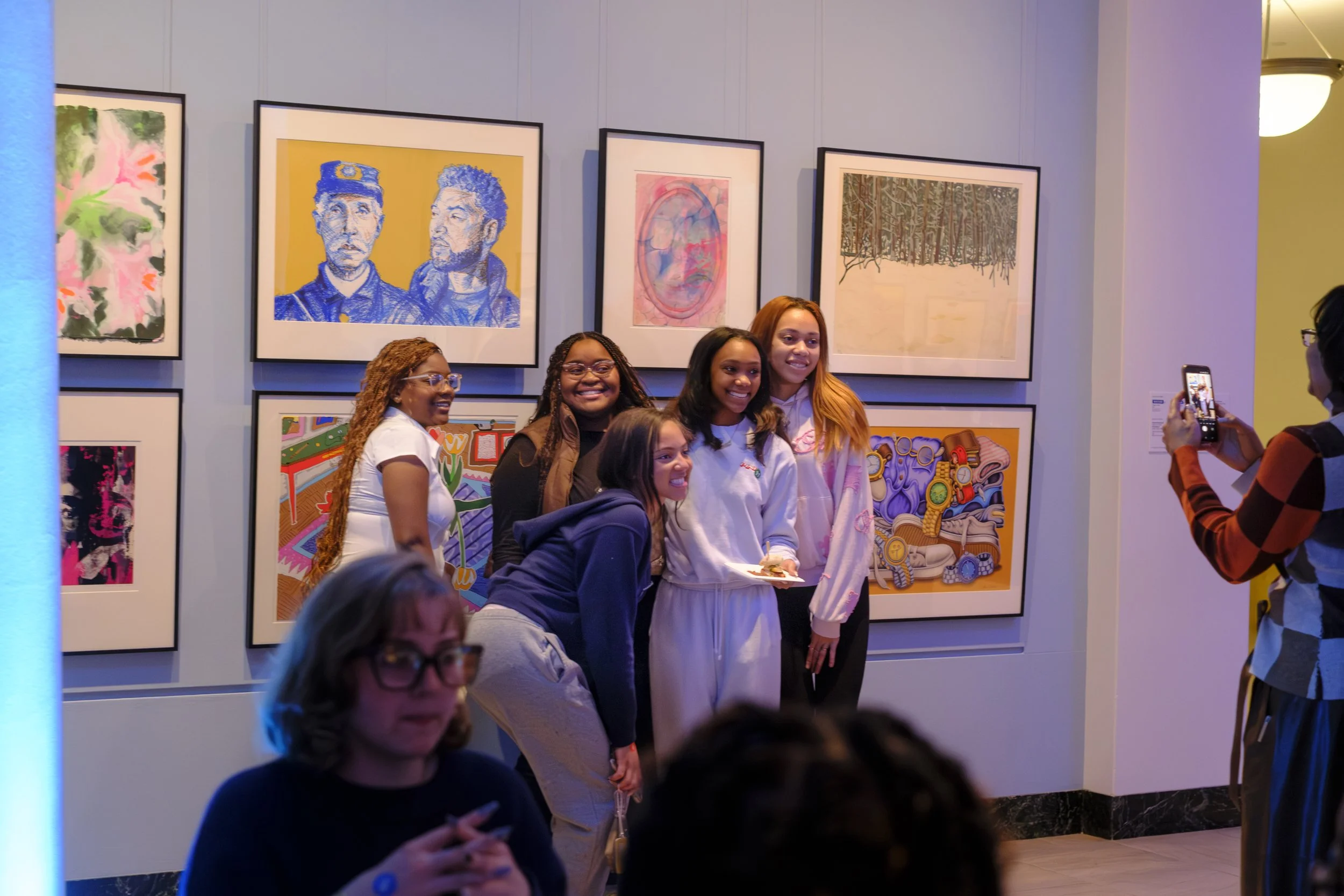 A group of five students stand together and pose for a photo in front of a wall of art.
