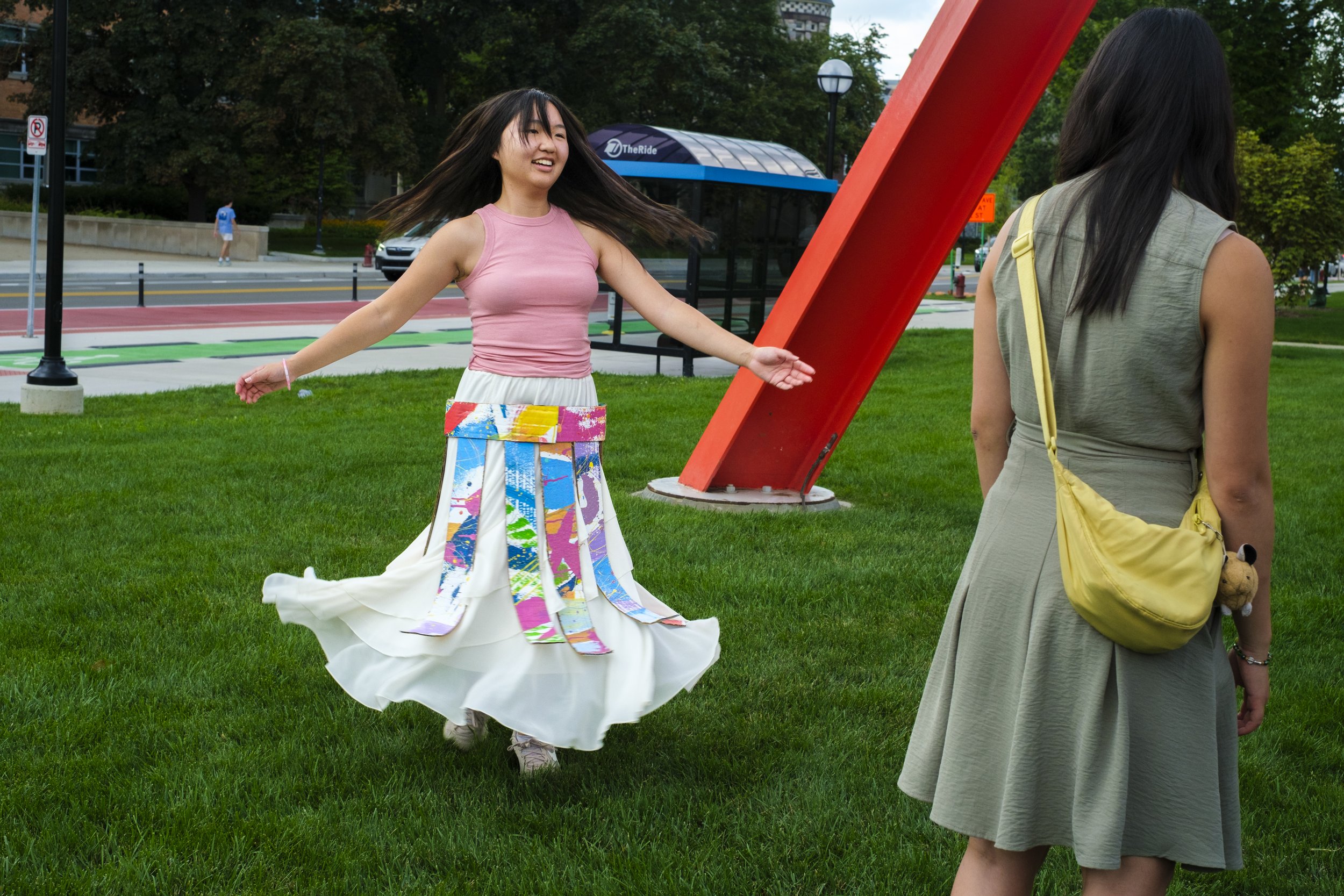 A young woman spins on a green lawn while wearing a cardboard skirt made in front of UMMA at the Festifools table at Artscapade..JPG