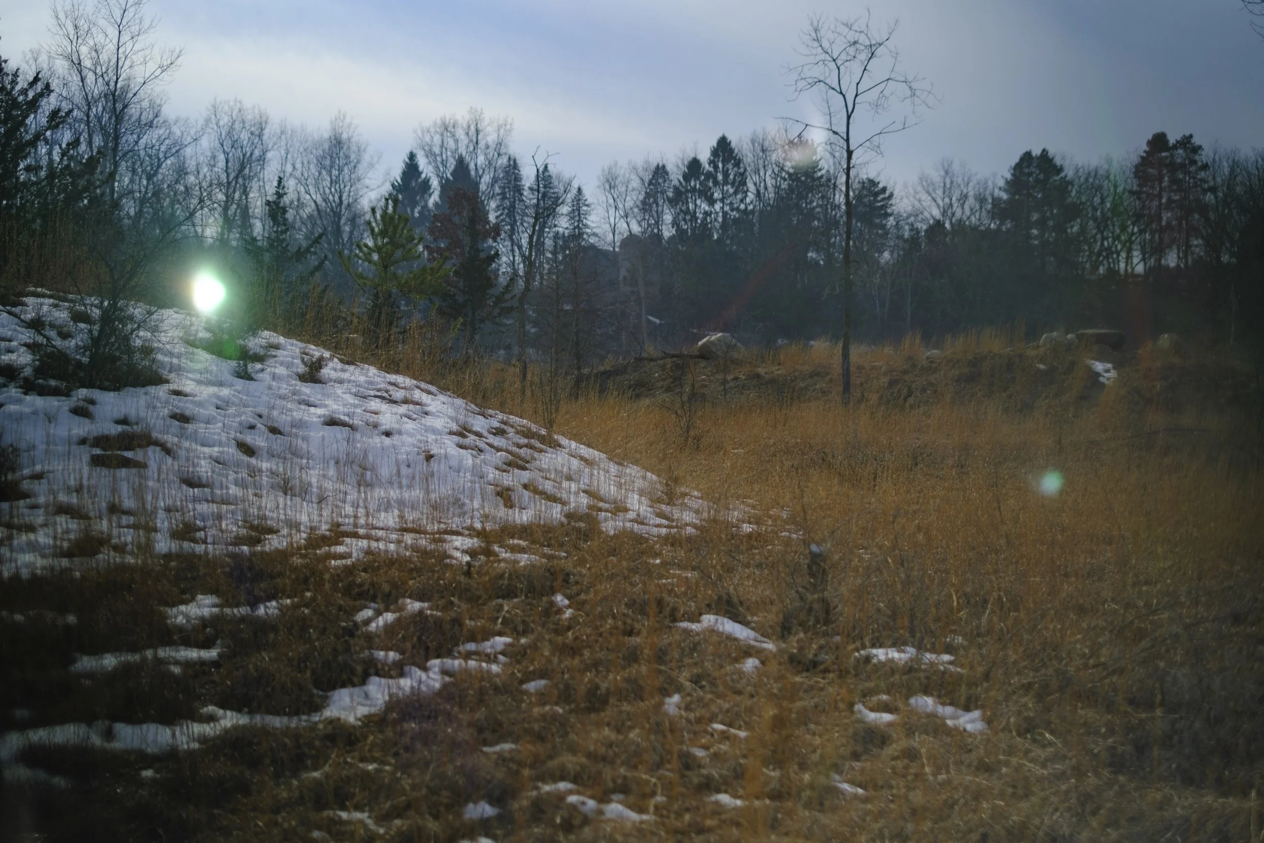 Hills with prairie grass and melting snow and two orbs of bright light.