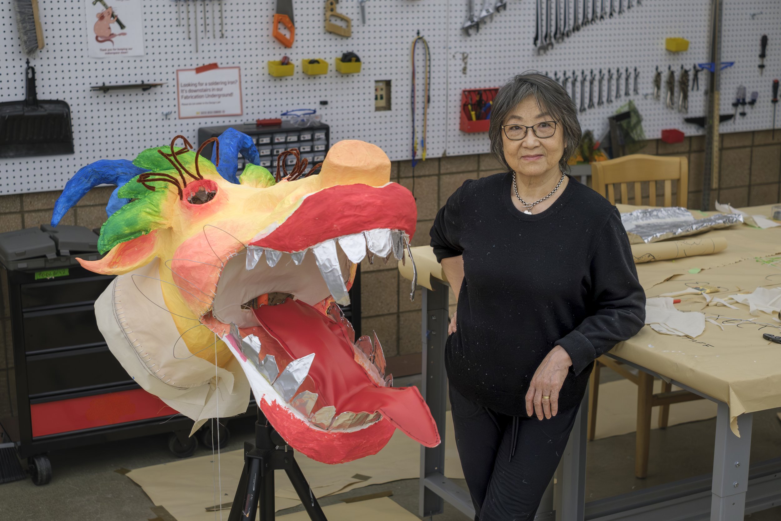 Artist Zhen Guo stands next to a dragon head art piece made out of recycled materials.