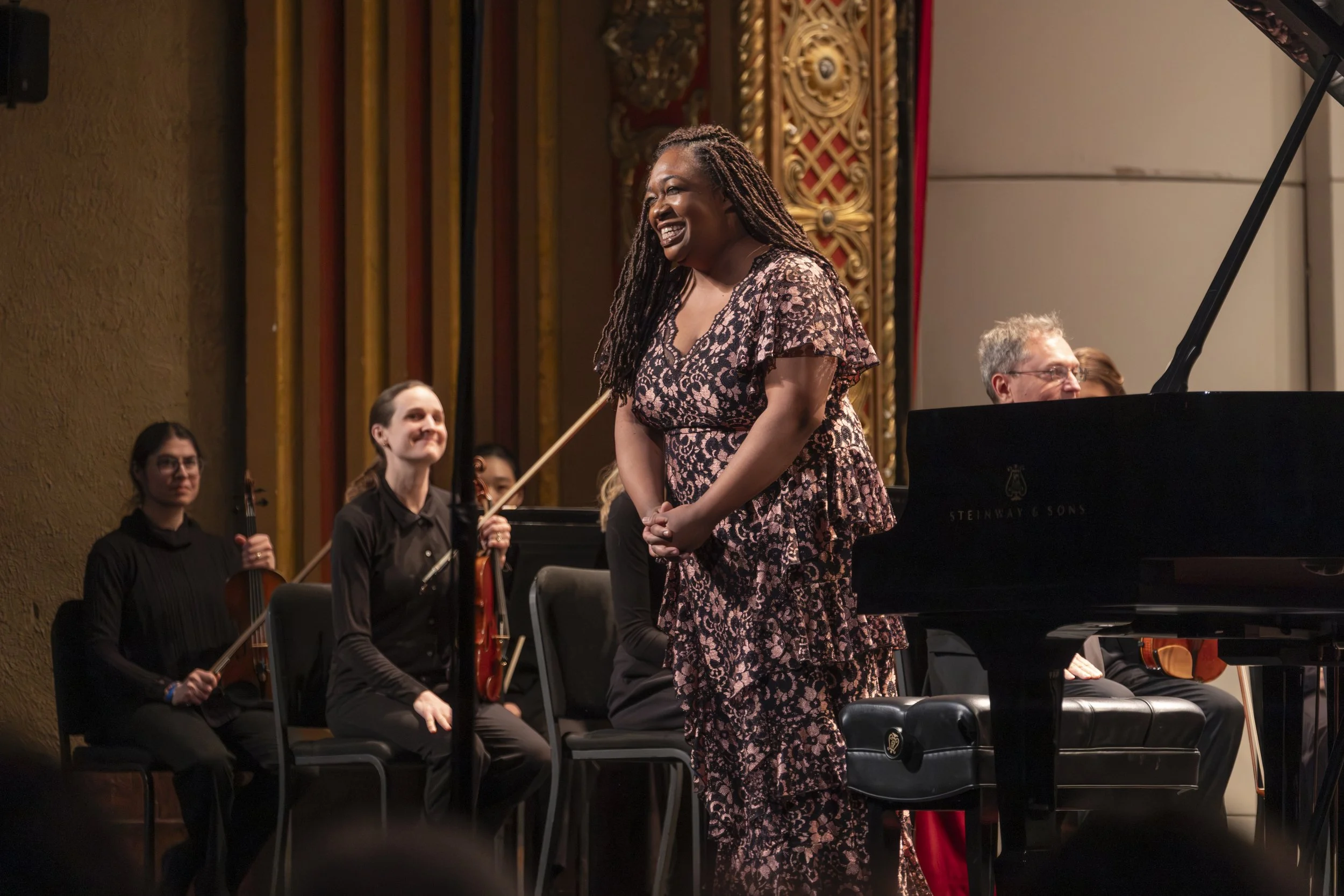Musician Michelle Cann stands on stage with violinist behind her smile.