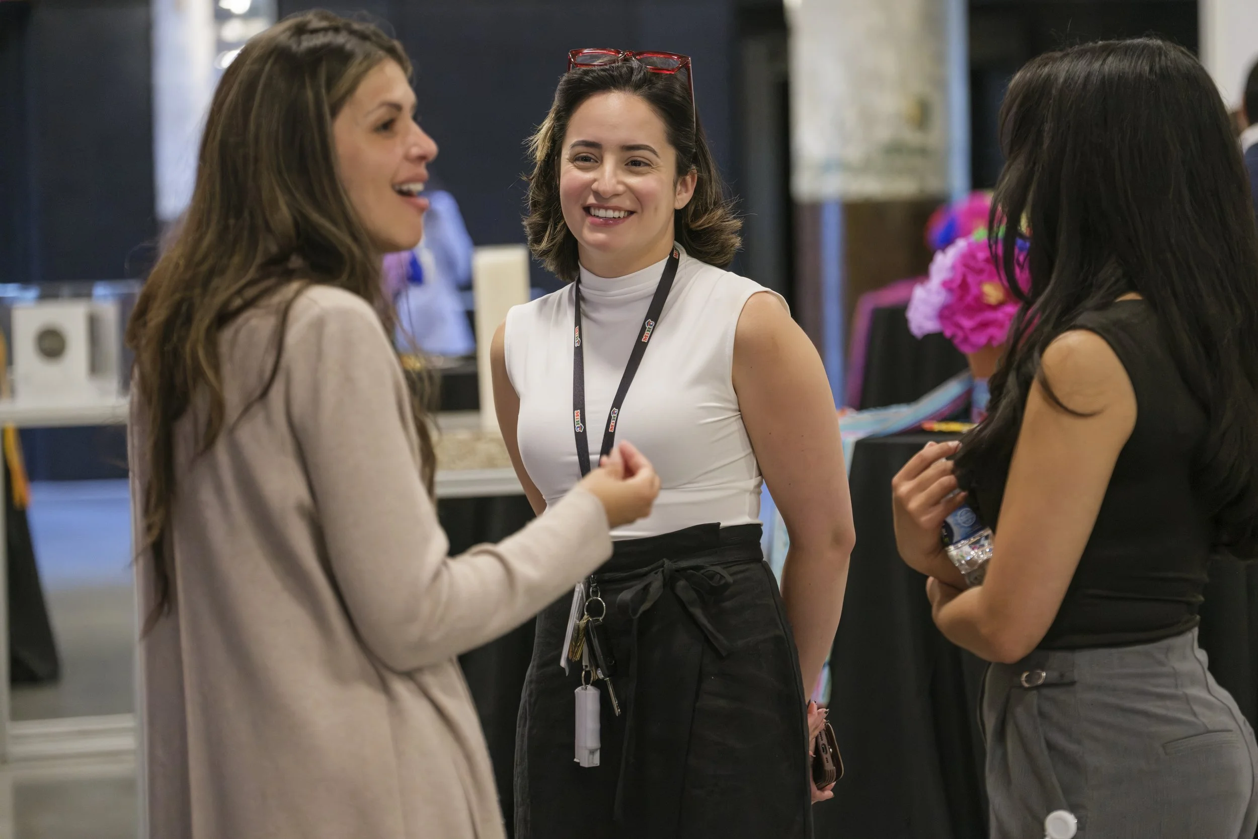 Three women smile at one another while talking to one another in a hallway.