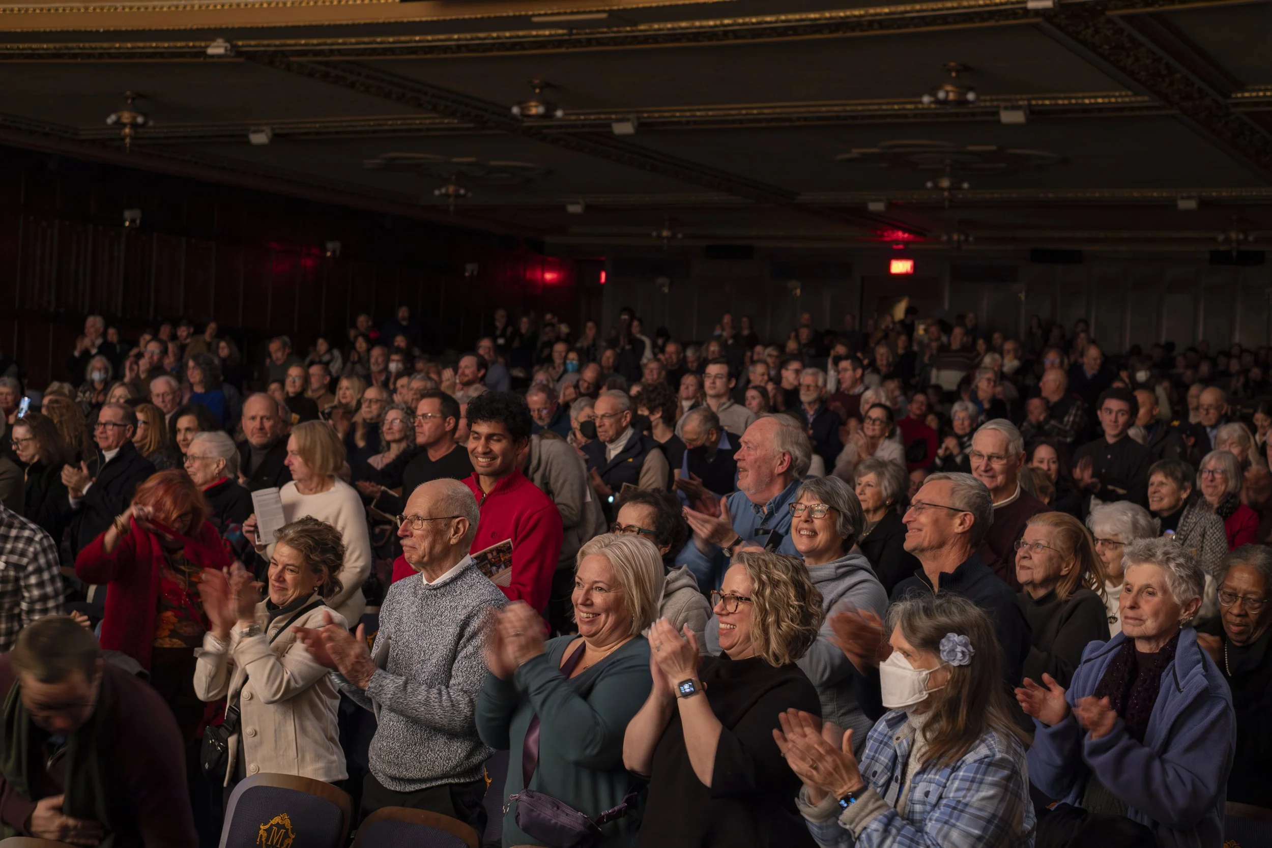 A large group of people stand and applaud in a theater.