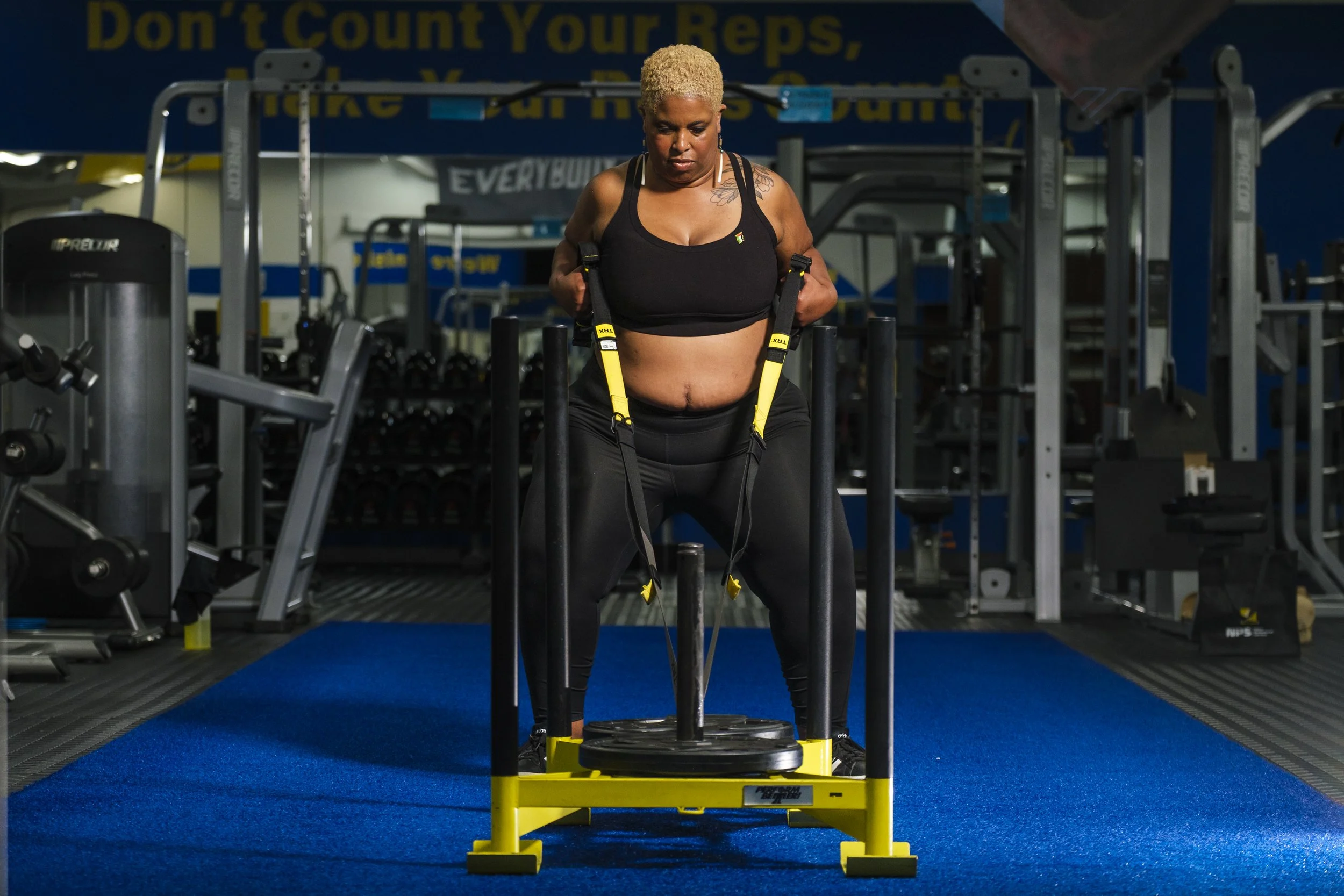 A woman focuses on using a weightlifting machine and ropes to pull it toward her during a weightlifting workout session in a gym.