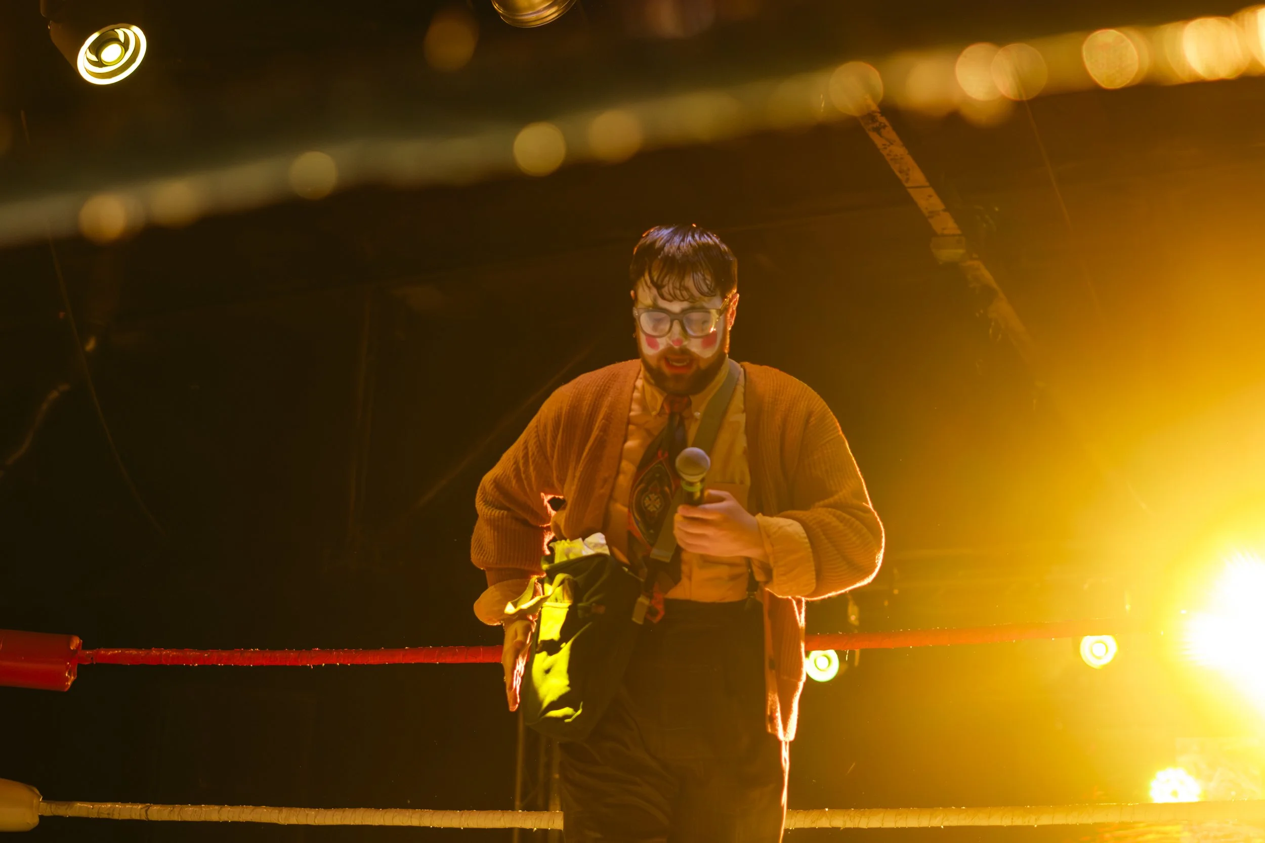 Clown therapist, Terry Piss, holds a microphone while standing in a wrestling ring.