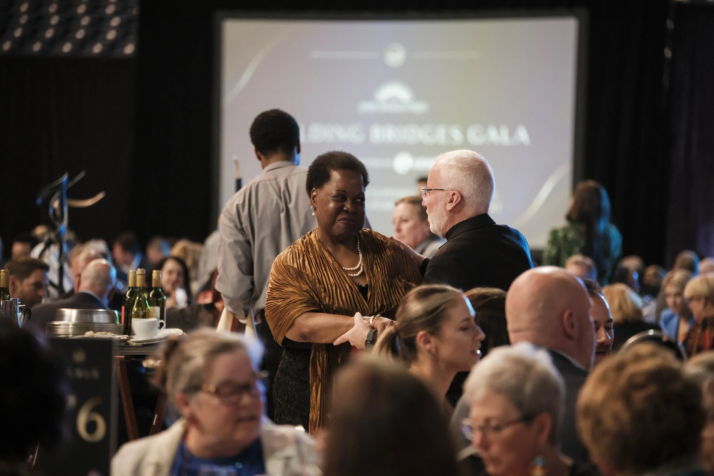 A woman smiles and holds hands with man during the Building Bridges Gala event.