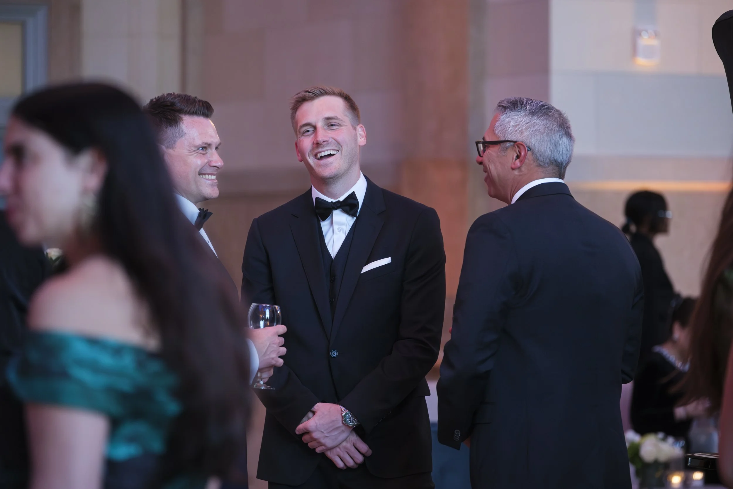 Three men smile at one another while wearing suits during the Ford Supplier Summit Awards at Michigan Central Station in Detroit.