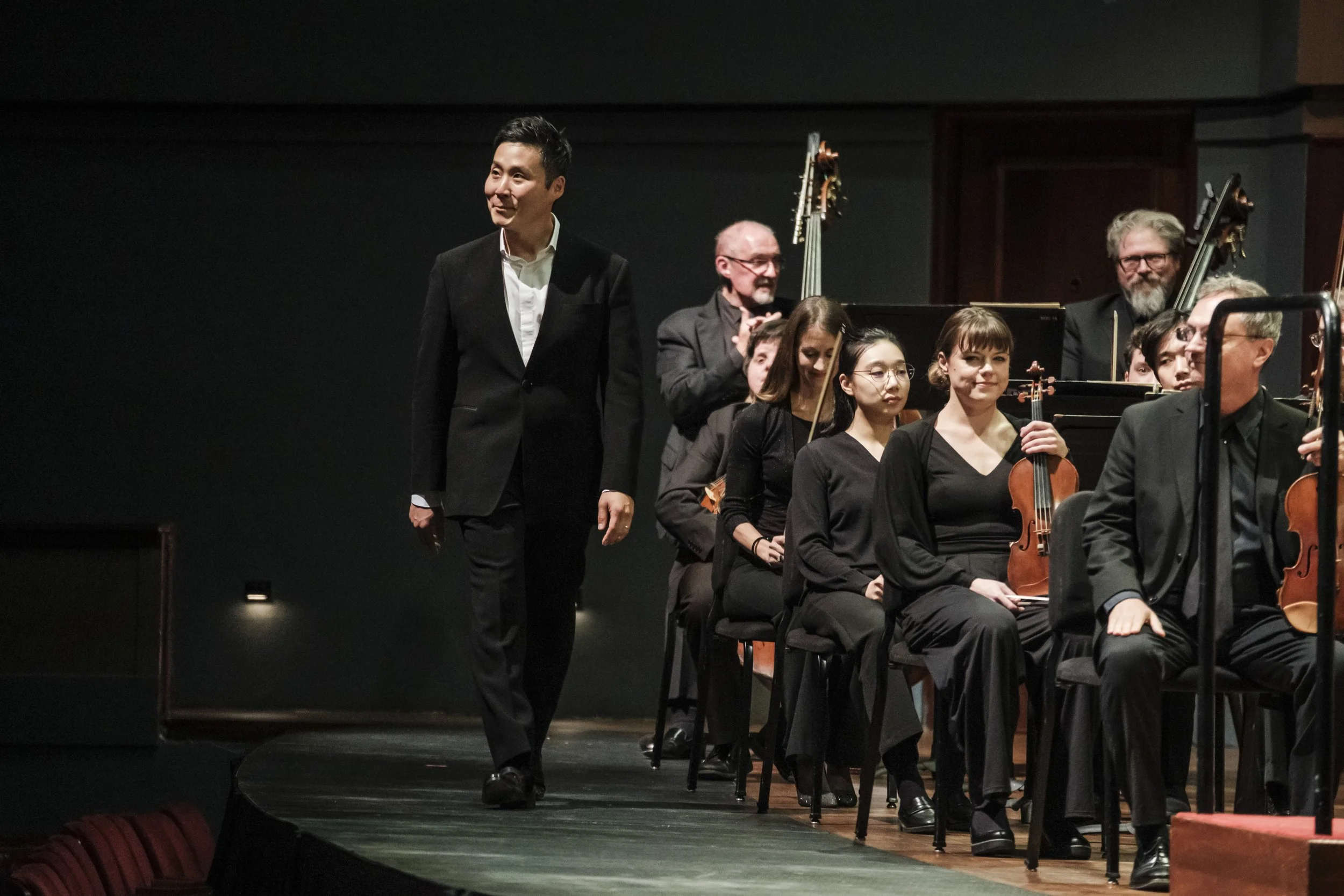 Ann Arbor Symphony Conductor, Earl Lee, looks out at the audience while he walks on stage in front of an orchestra.