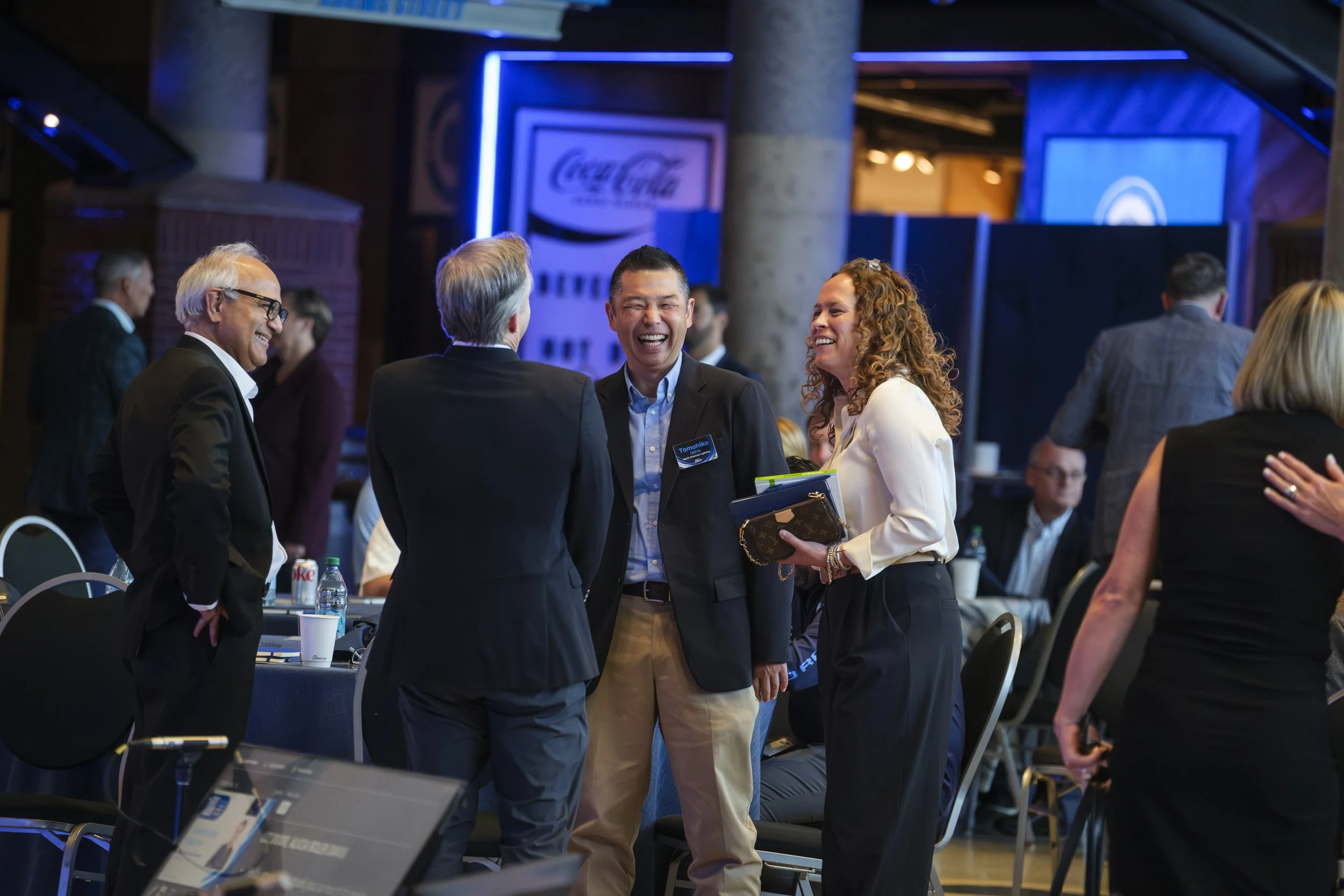 A group of four people stand around and smile at one another with blue tables in the background.