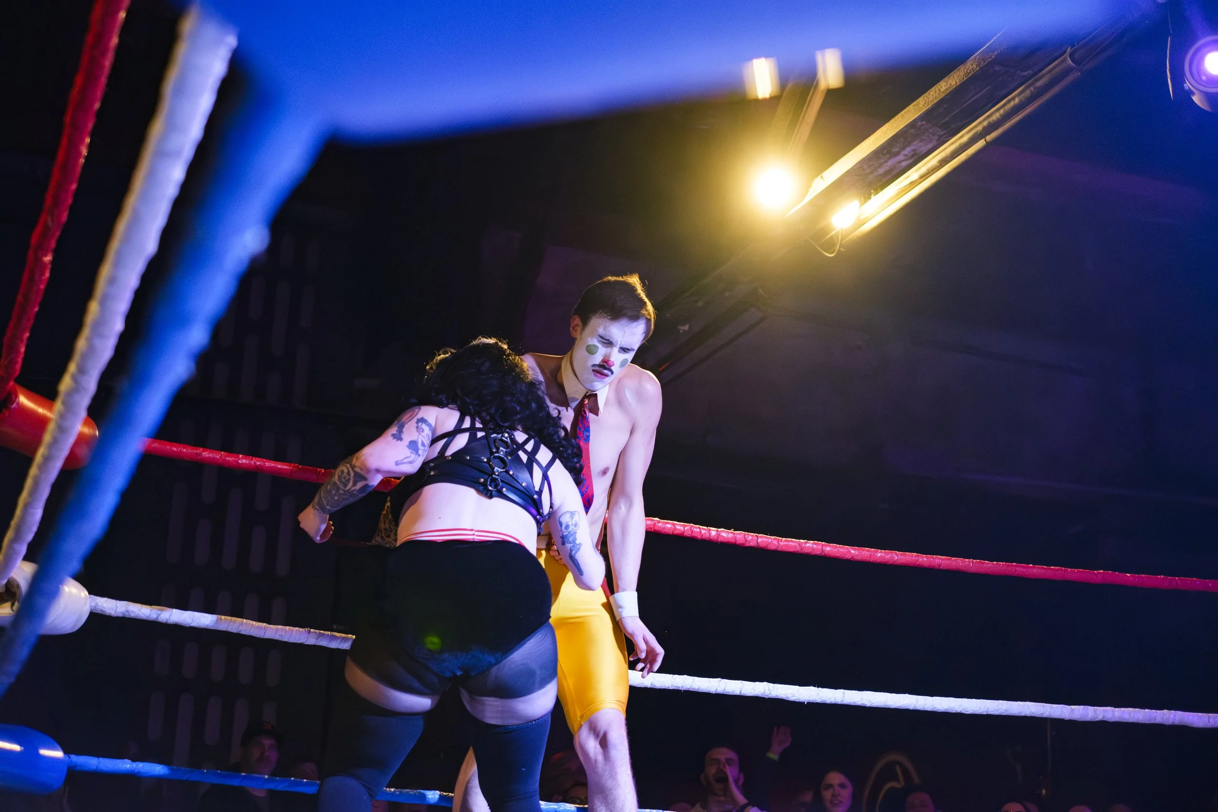 Clown wrestler, Generous James, is punched by his opponent, Rusty Busches, in a wrestling ring.