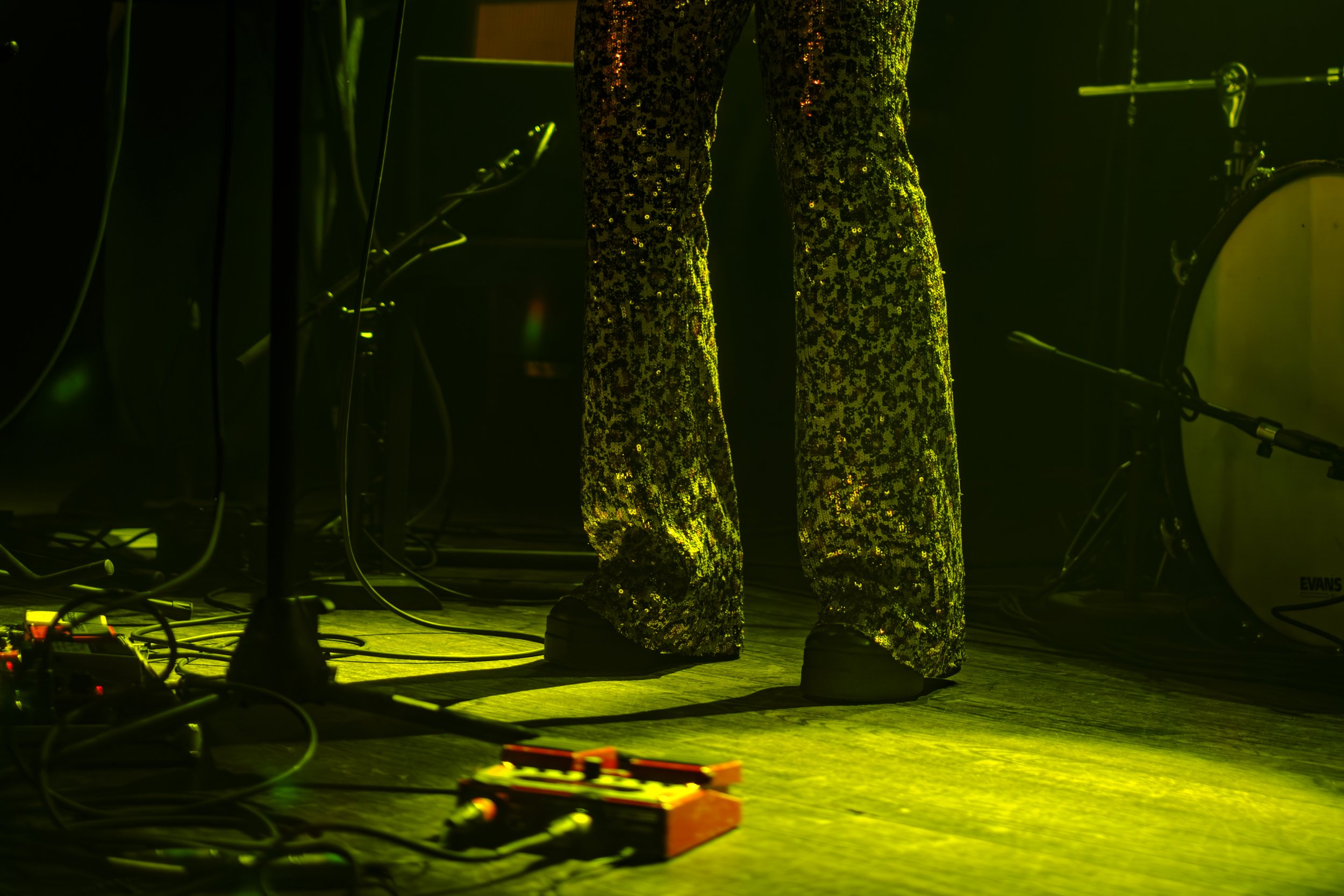 Sequin Pants are illuminated by lime-green concert lighting on a wooden stage.
